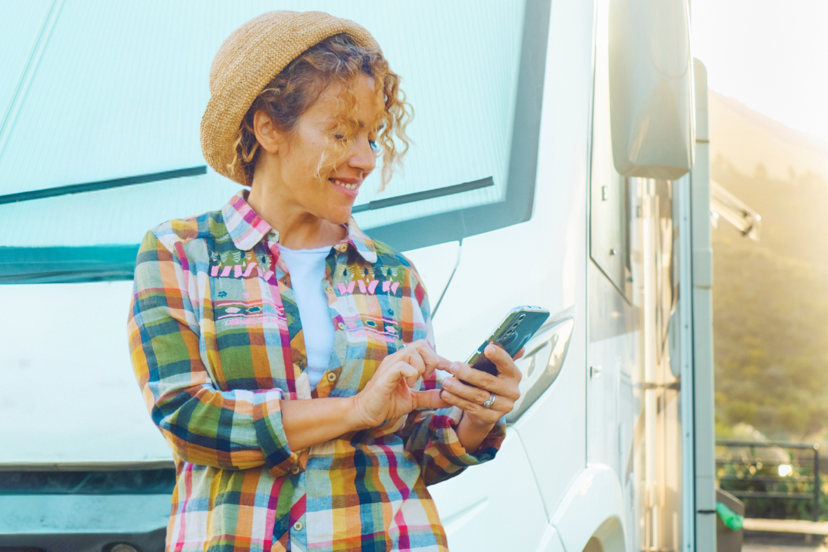 Frau steht vor einem Wohnmobil und schaut auf ihr Smartphone