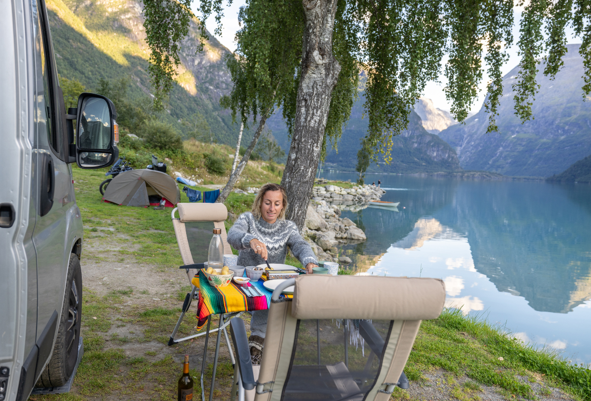 Eine Frau geniesst ihr Frühstückt neben ihrem Camper.