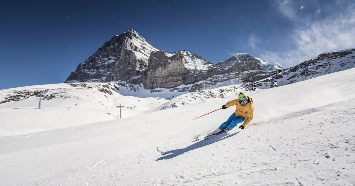 Skifahrer, der einen steilen Abhang hinunterfährt Bild von unten aufgenommen mit einem grossen Berg im Hintergrund