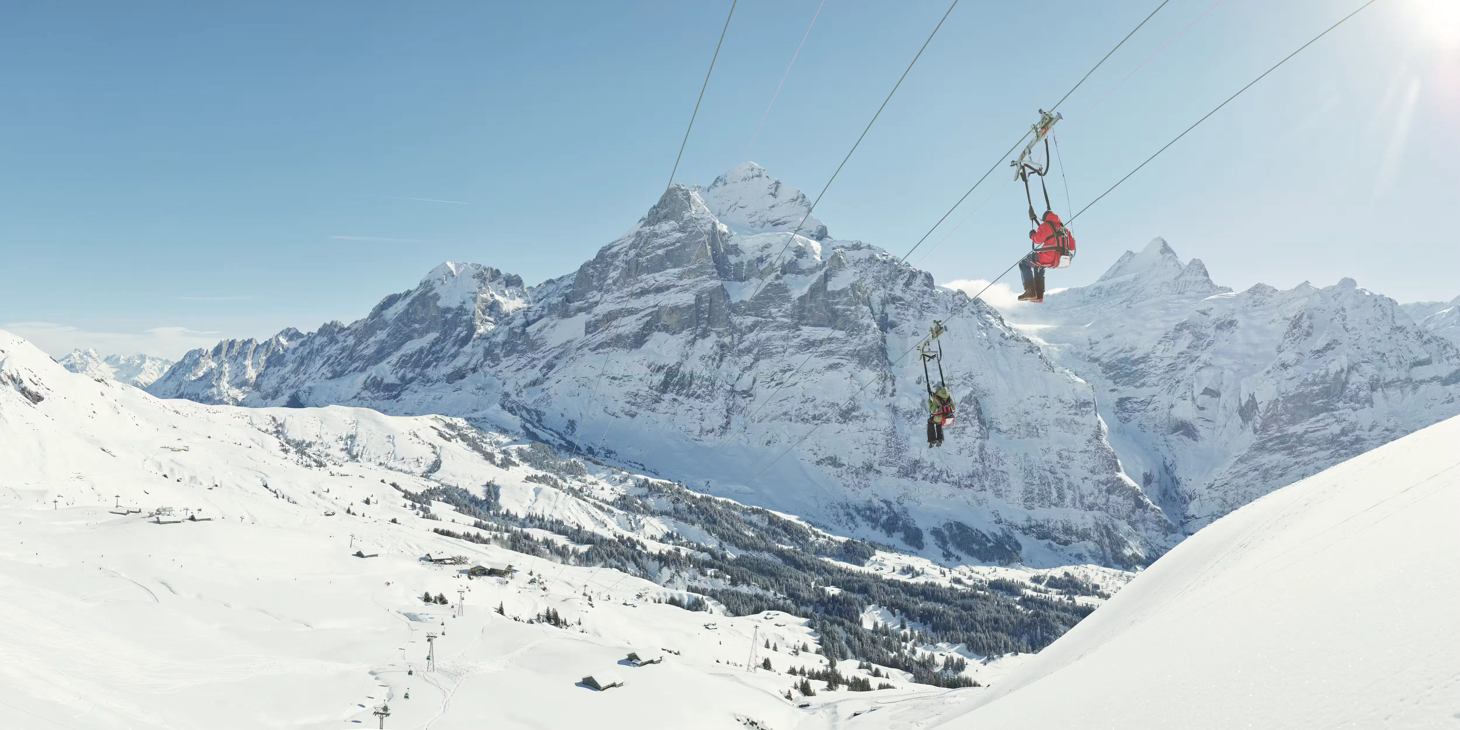zwei Personen, die eine Zip-Line in Winer hinunterrutschen, mit schöner Berglandschaft im Hintergrund