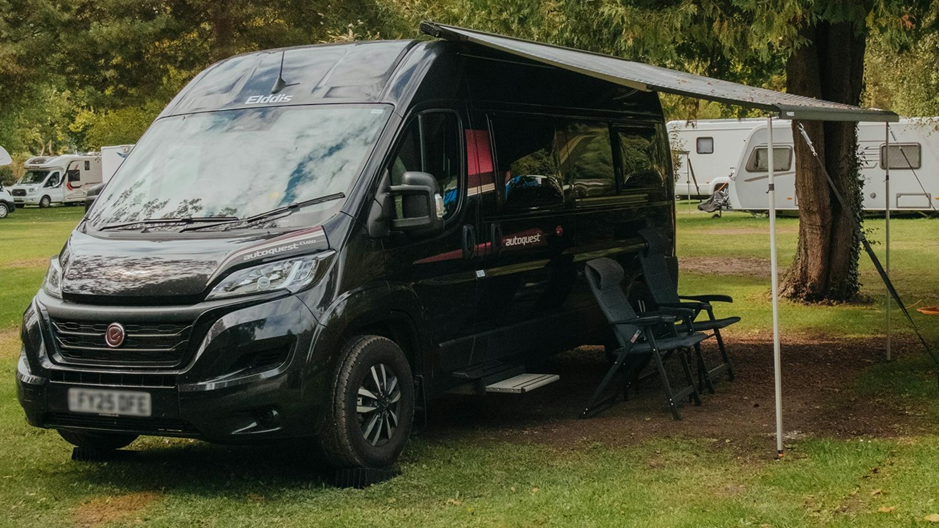 Kastenwagen steht auf einem Stellplatz mit offener Markise und zwei Campingstühlen darunter