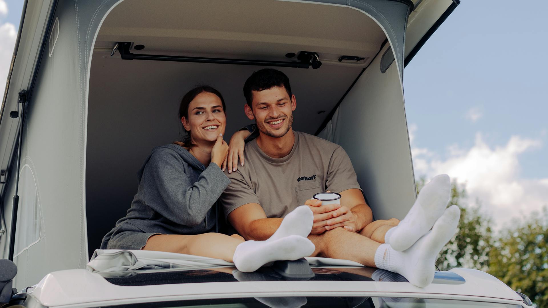 Frau und Mann sitzt in offenem Aufstelldach von Volkswagen California