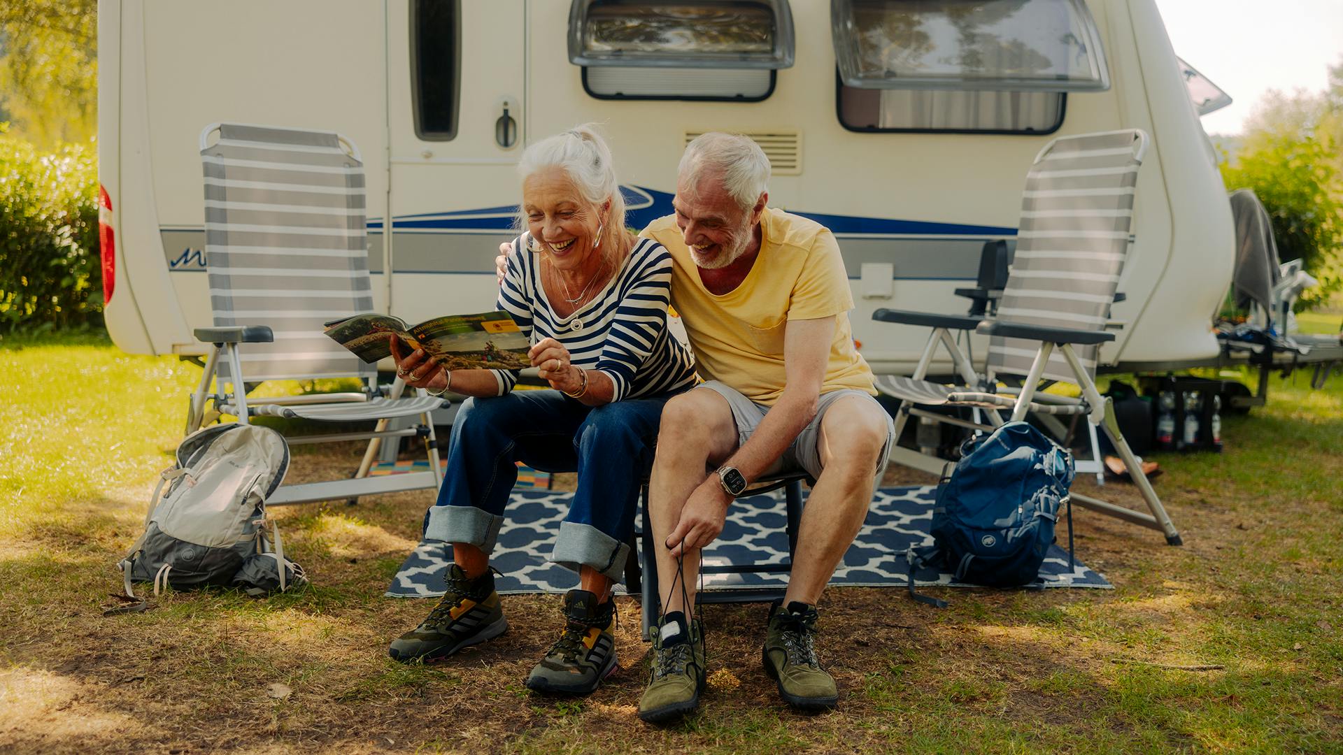 Älteres Paar sitzt mit Wanderschuhen und Wanderkarte vor Wohnwagen