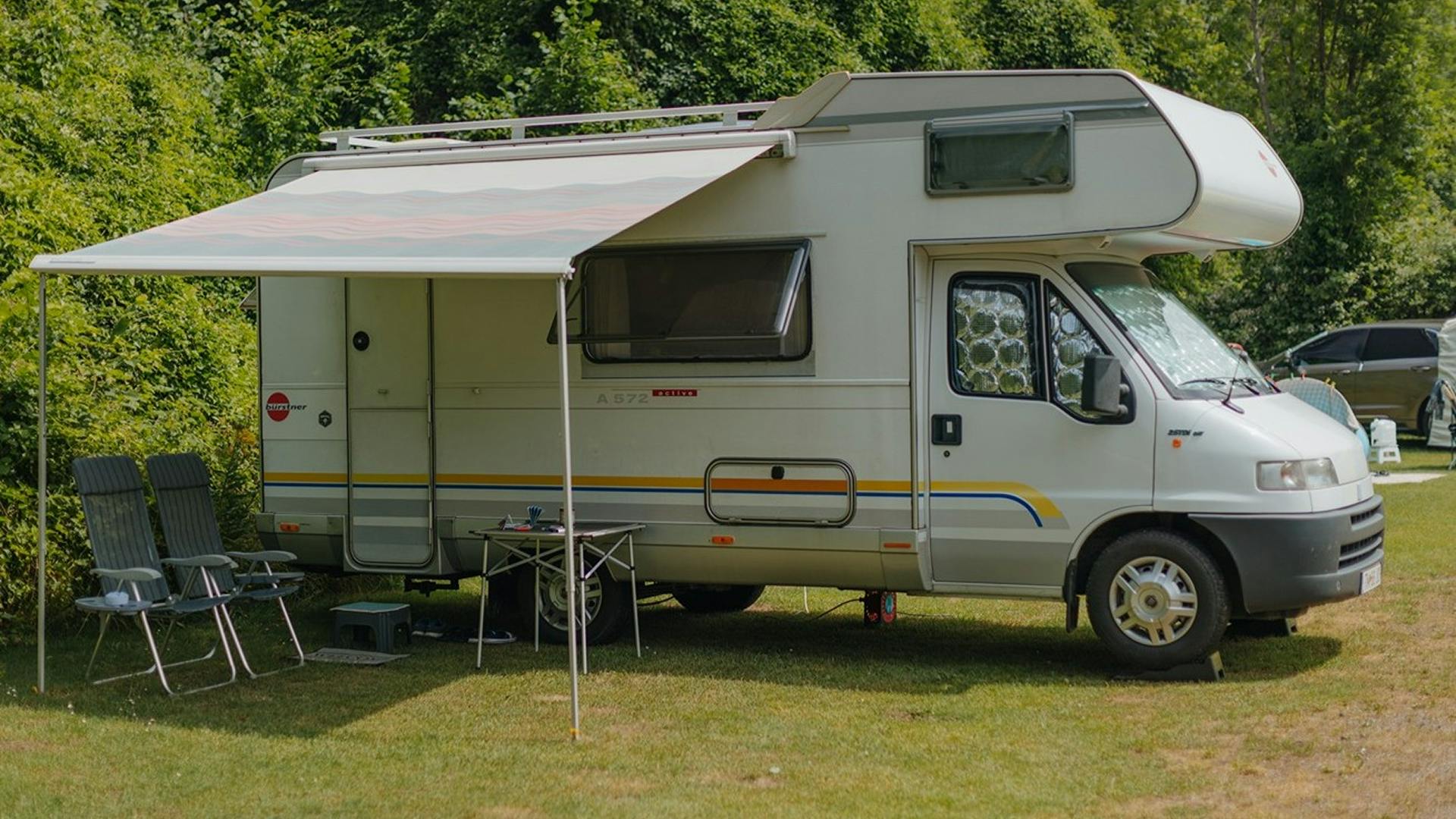 Wohnmobil mit offener Markise und zwei Campingstühlen und Tisch darunter
