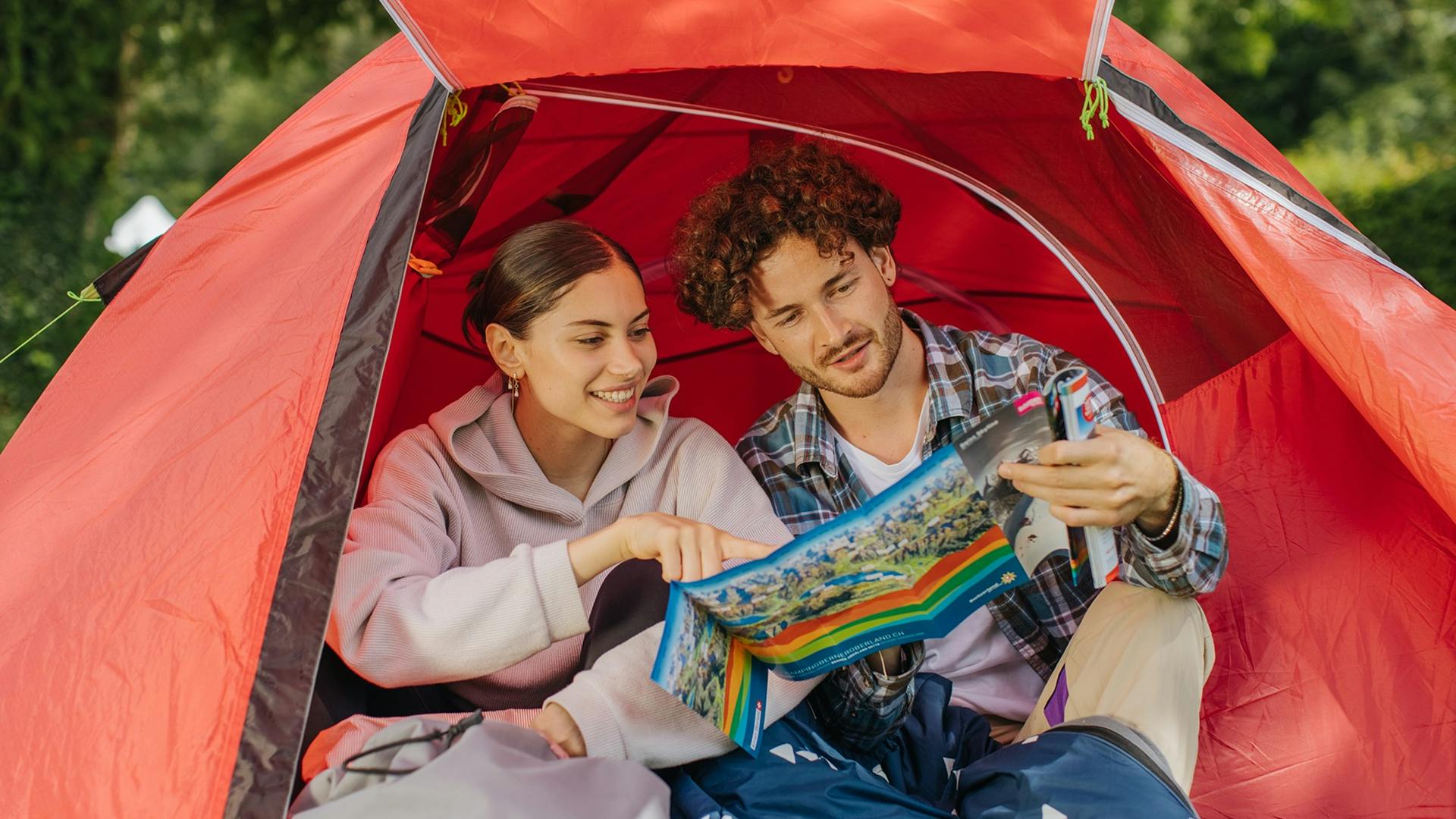 Frau und Mann sitzen in rotem Zelt und schauen auf eine Wanderkarte
