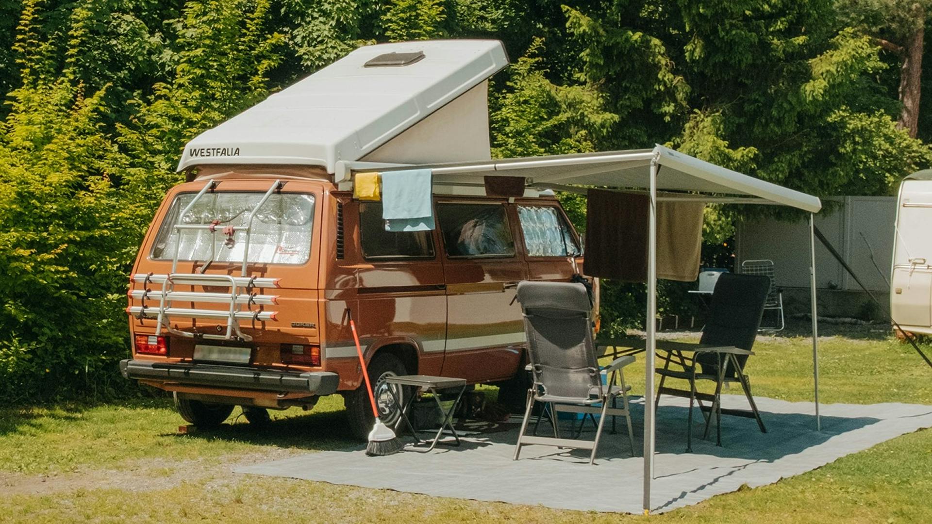 Alter Volkswagen Van mit Aufstelldach und Markise sowie zwei Campingstühlen und Tisch auf einem Stellplatz