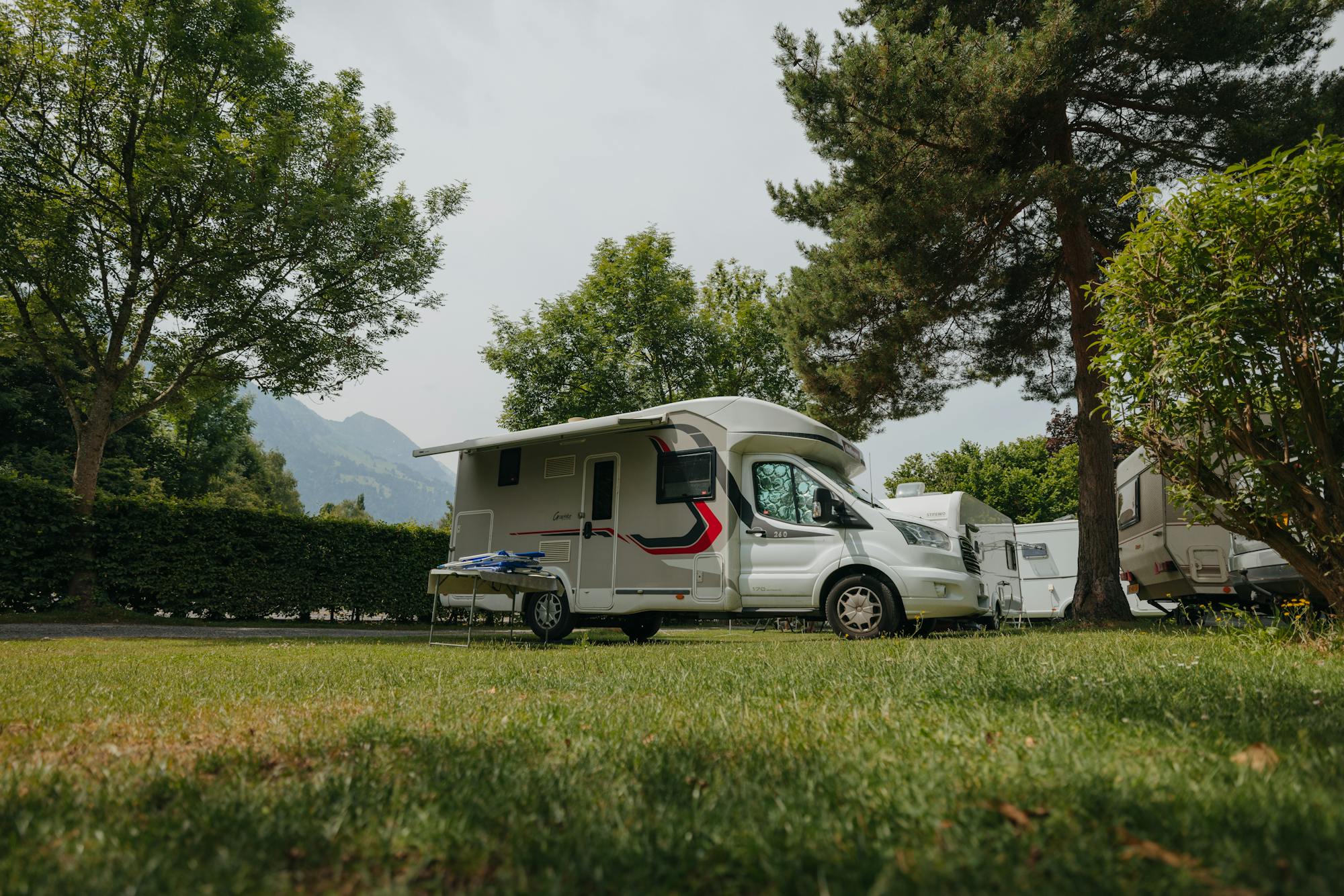 Stellplatz auf dem Camping Alpenblick mit Wohnmobil und schönem Baumbestand rundherum, Berge im Hintergrund
