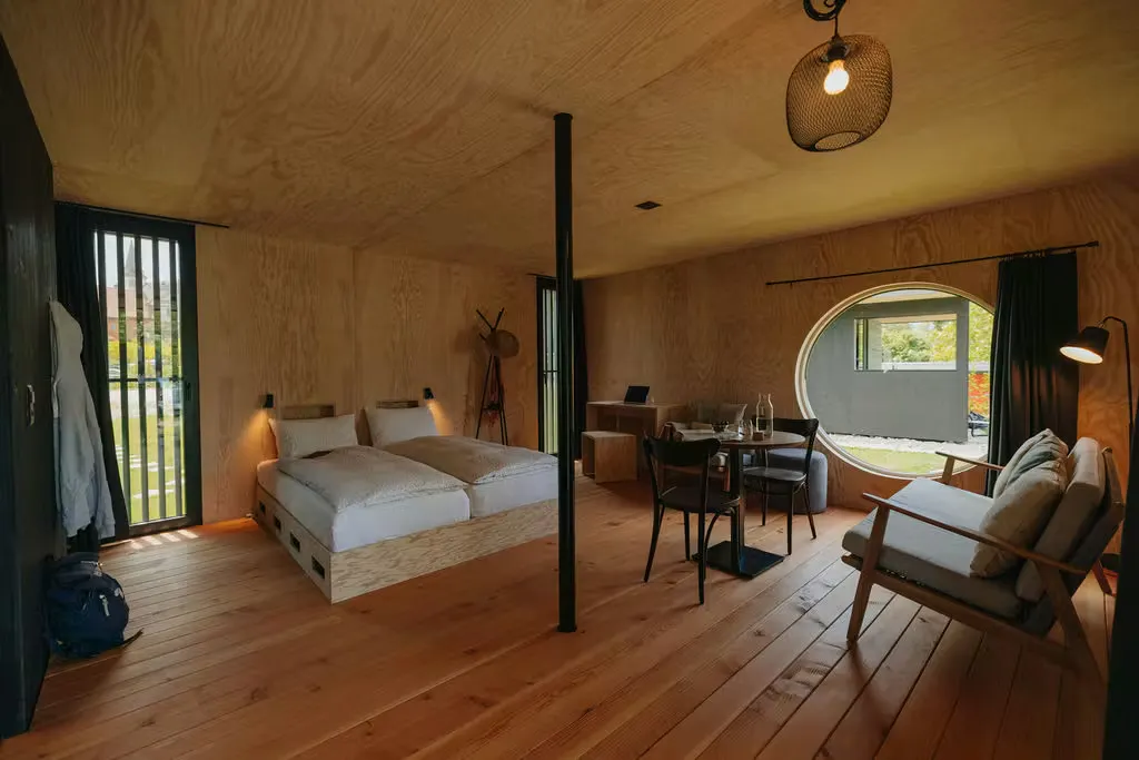 Innenansicht der Mietunterkunft Beach Loft auf Camping Erlach mit Doppelbett in der Mitte, Sitzmöglichkeiten und grossen Fenstern