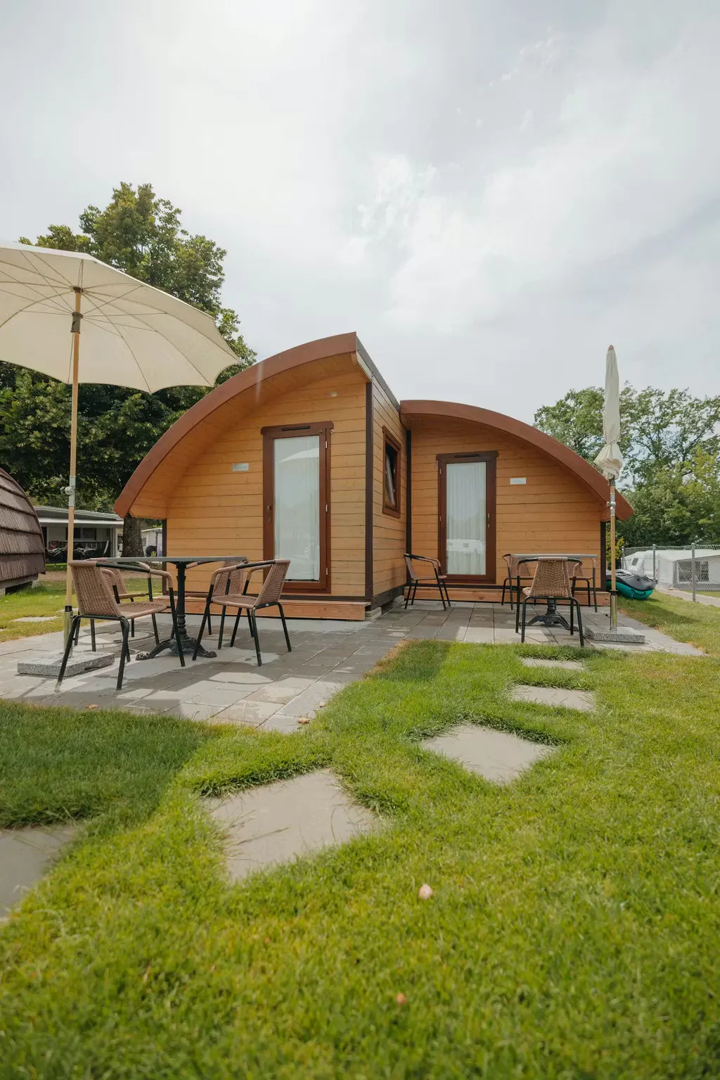 Beach Cabin Unterkunft von aussen mit Tisch und Stühlen und einem Sonnenschirm im Freien, umgeben von grünem Gras
