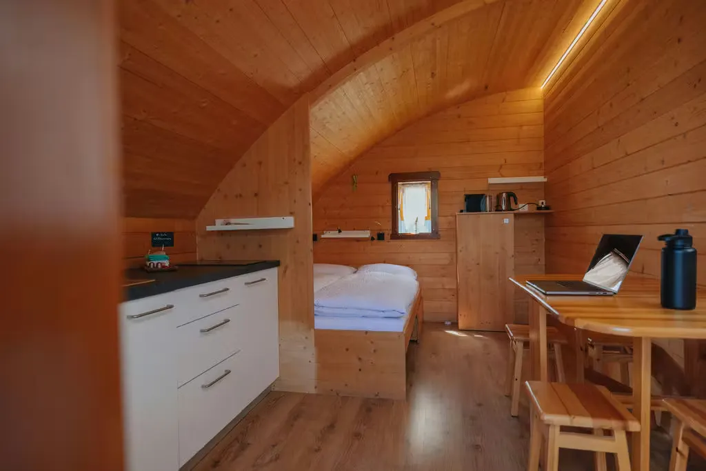 Innenansicht der Mietunterkunft Beach Cabin auf Camping Erlach mit Doppelbett, kleinem Tisch und Stühlen und Küchenzeile, alles aus Holz