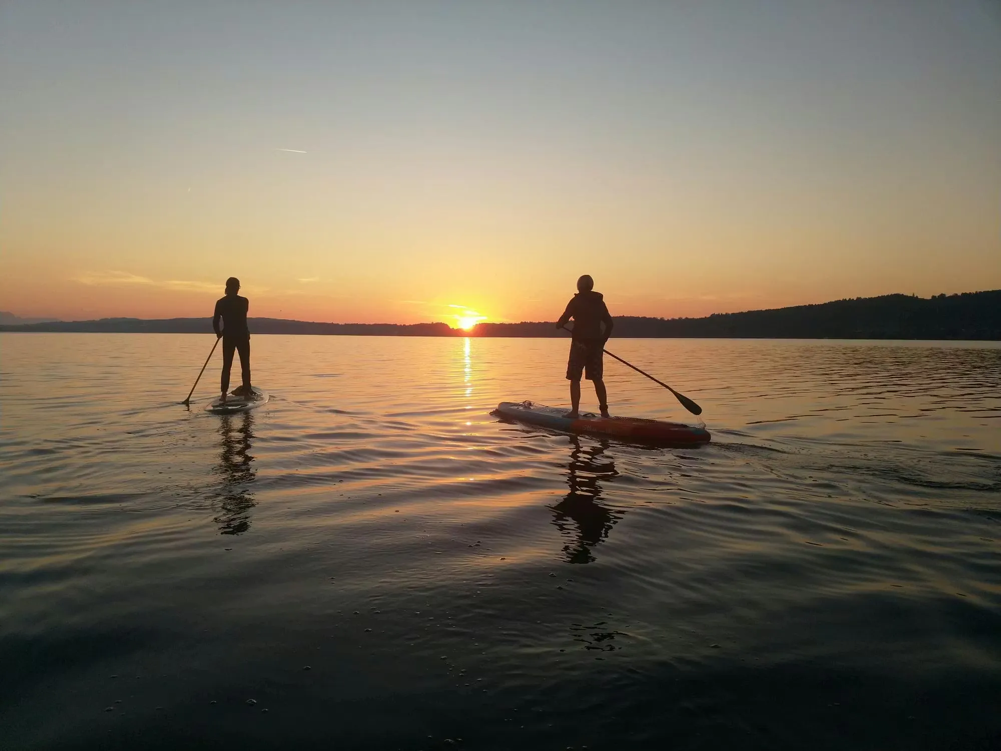 Zwei Stand-Up Paddler bei Sonnenuntergang auf dem See