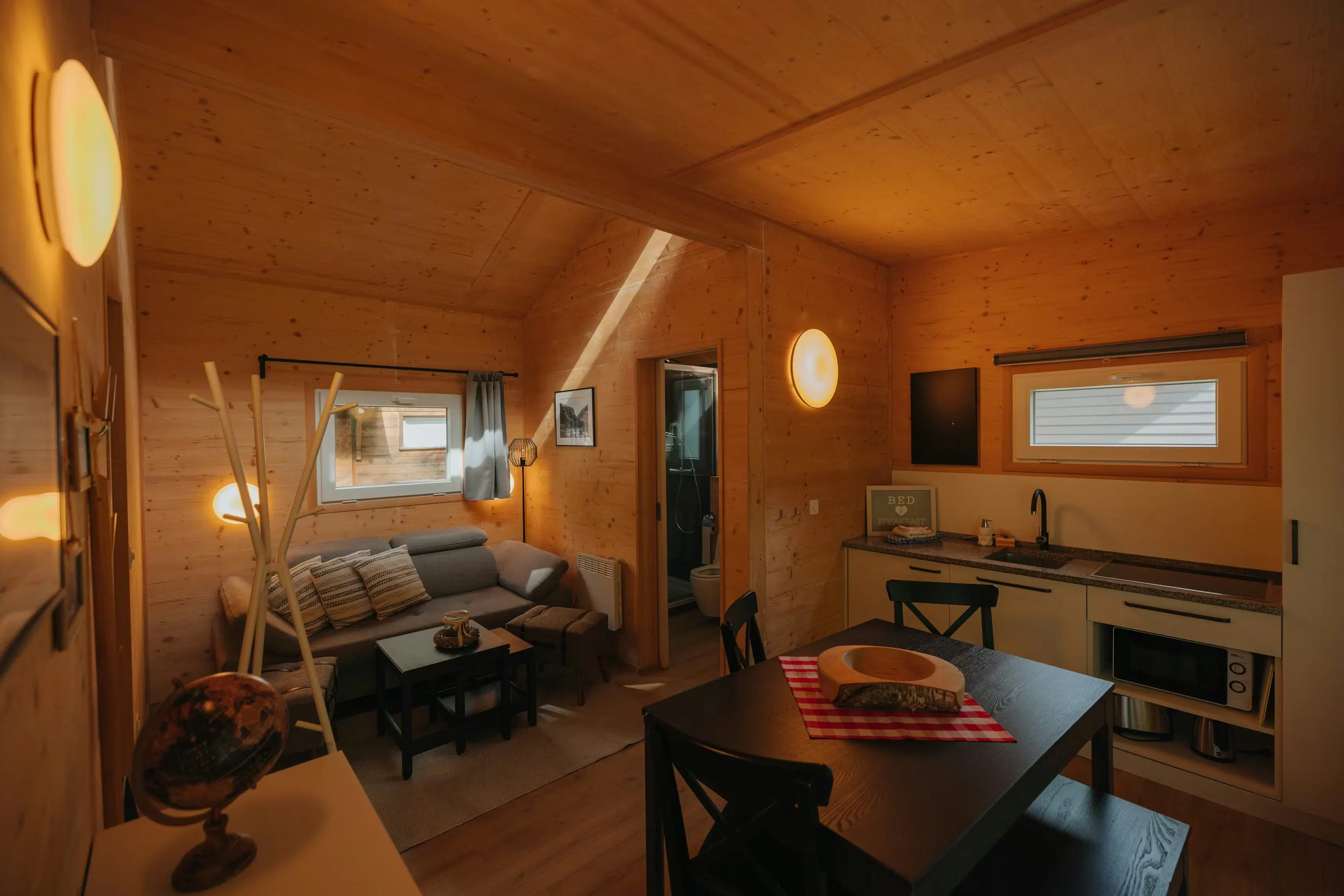 Wohnzimmer mit kleiner Küchenzeile, Tisch mit 4 Stühlen und einem Sofa in einer Holzkabine mit Blick in Richtung Bad