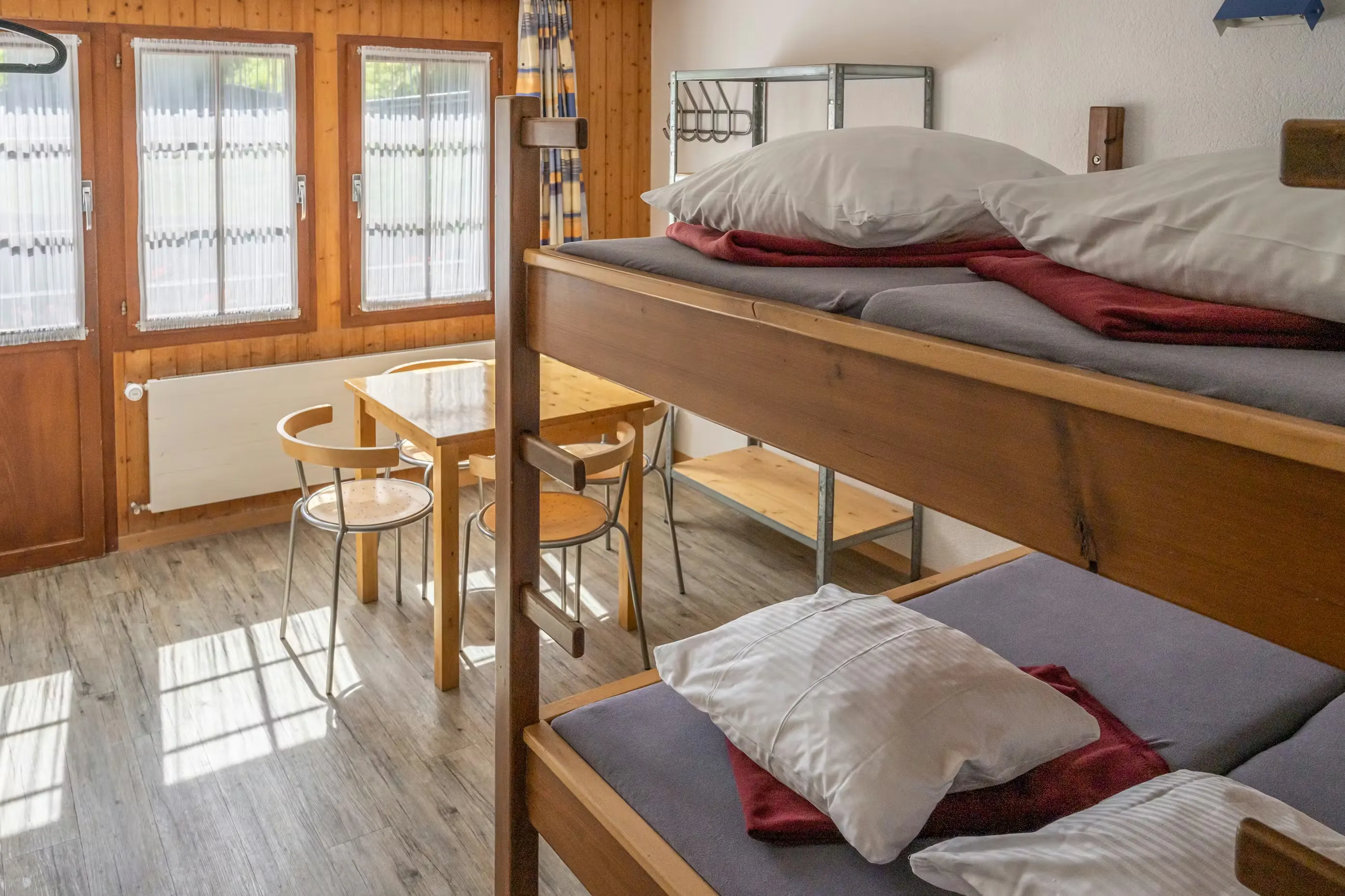 Herbergszimmer mit einem Doppelstockbett, einem Tisch mit vier Stühlen und einem Kleiderschrank