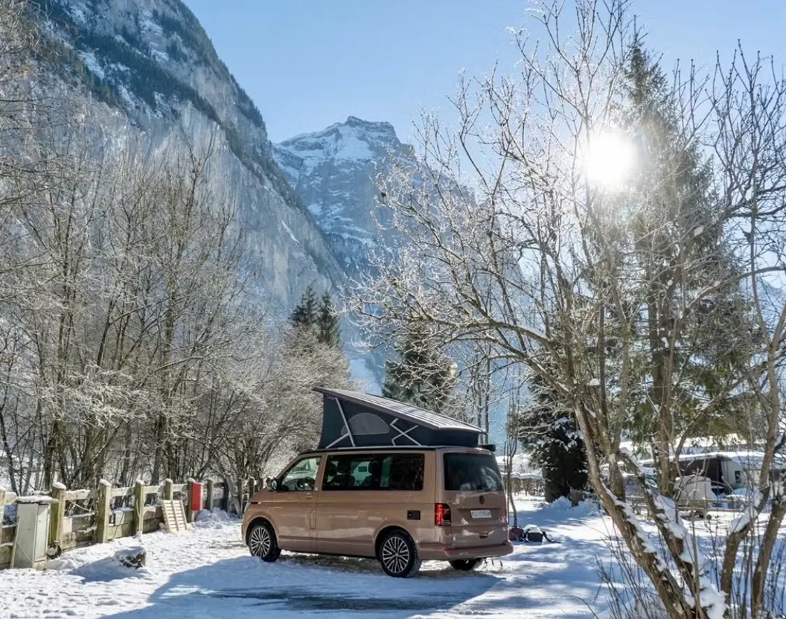 Volksvagen California auf einem verschneiten Stellplatz Classic im Lauterbrunnental bei strahlendem Sonnenschein