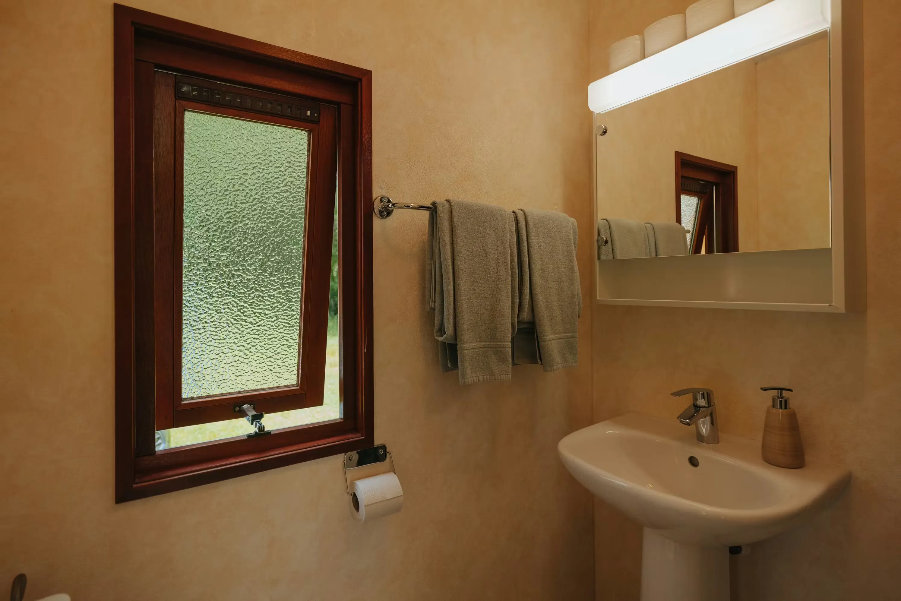 Badezimmer des Mobilheims Jungfrau mit einem Waschbecken und einem kleinen Fenster an der Seite, zwei Handtücher hängen an der Wand