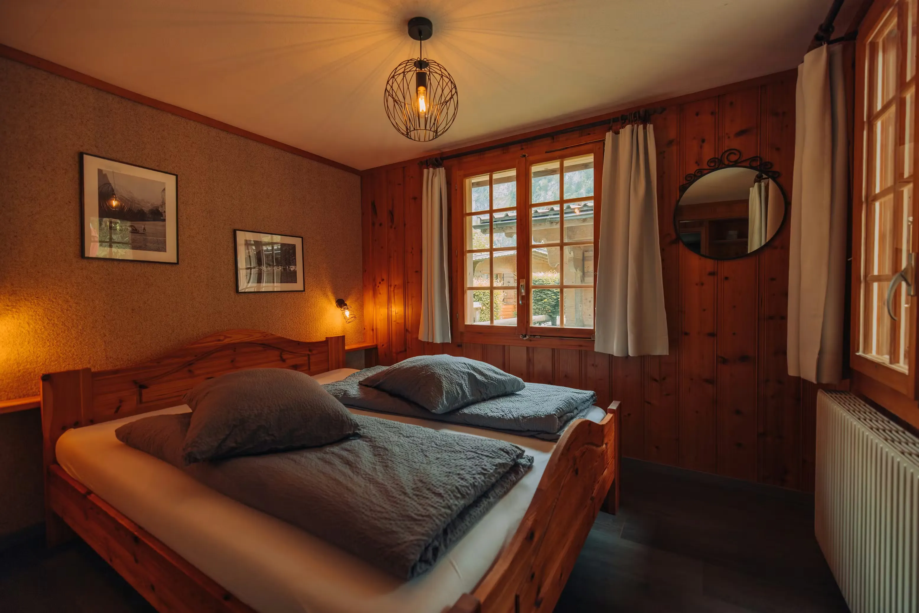 Schlafzimmer in einer Holzhütte mit Doppelbett, grauen Laken und zwei alten gerahmten Fotos an der Wand