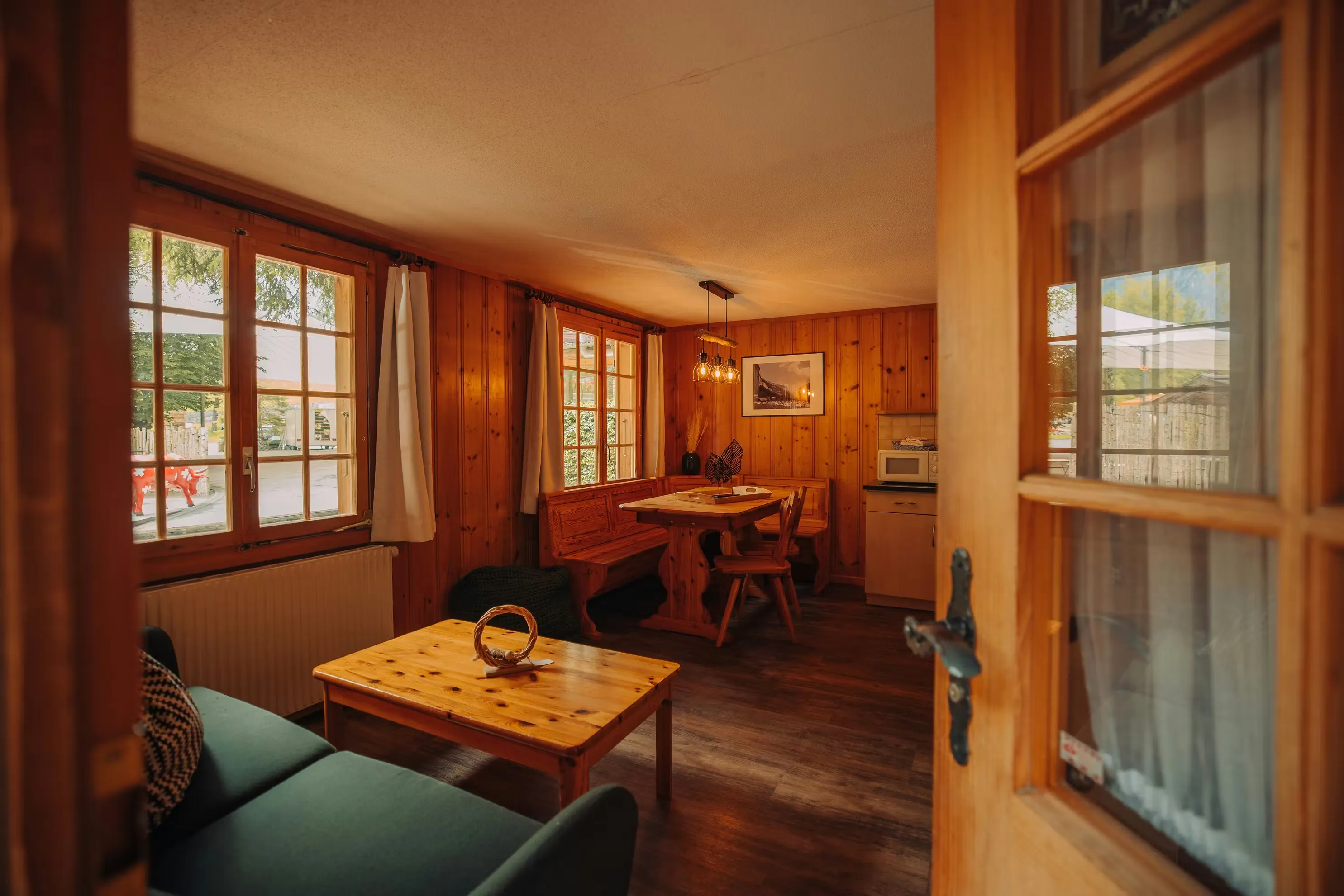 Blick in ein Wohnzimmer einer hölzernen Winterhütte mit Sofa und einem Ecktisch mit einer Bank und zwei Stühlen
