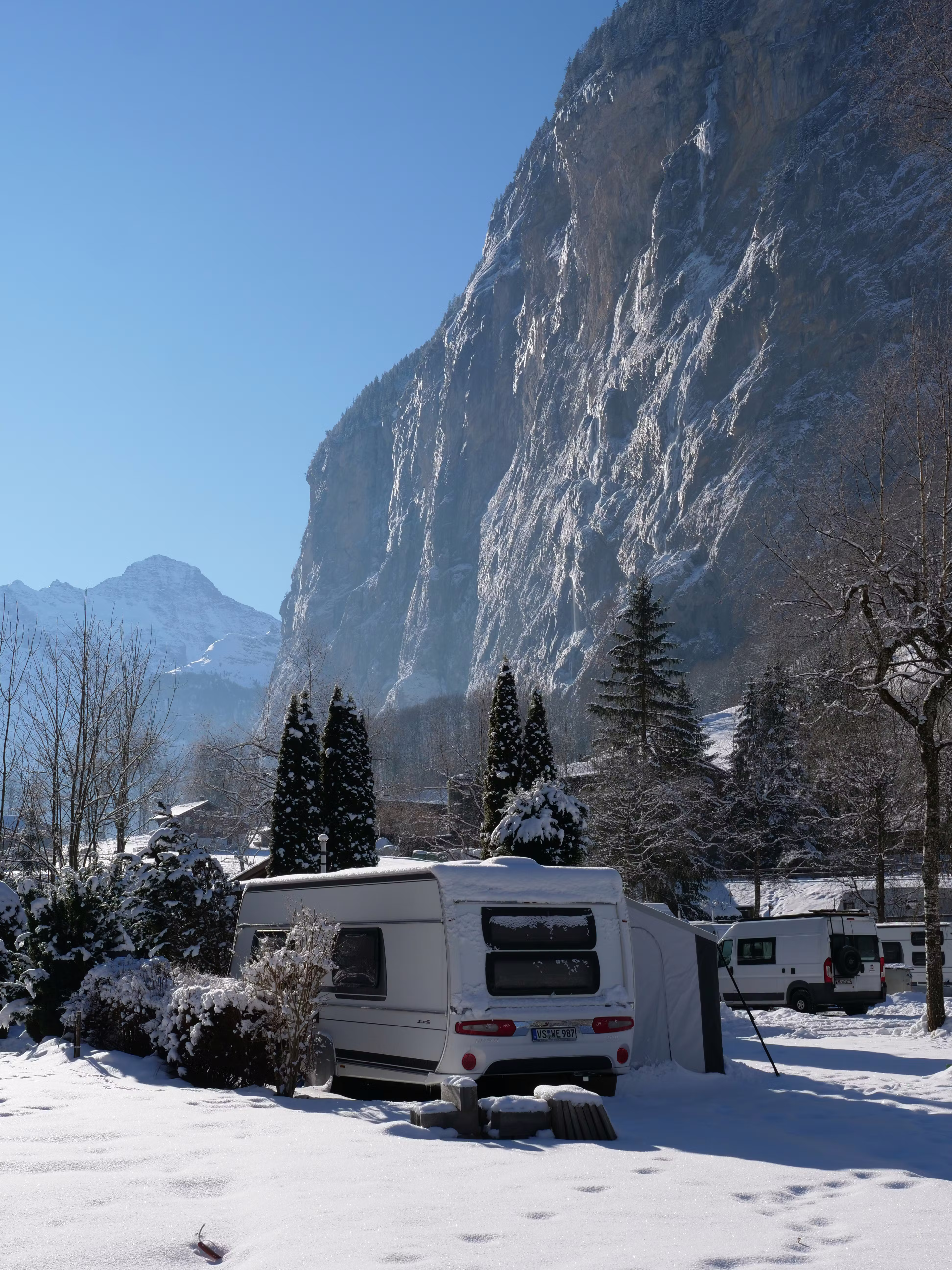 Wohnwagen im Winter auf dem Camping Jungfrau im Lauterbrunnental mit Felswänden und blauem Himmel im Hintergrund