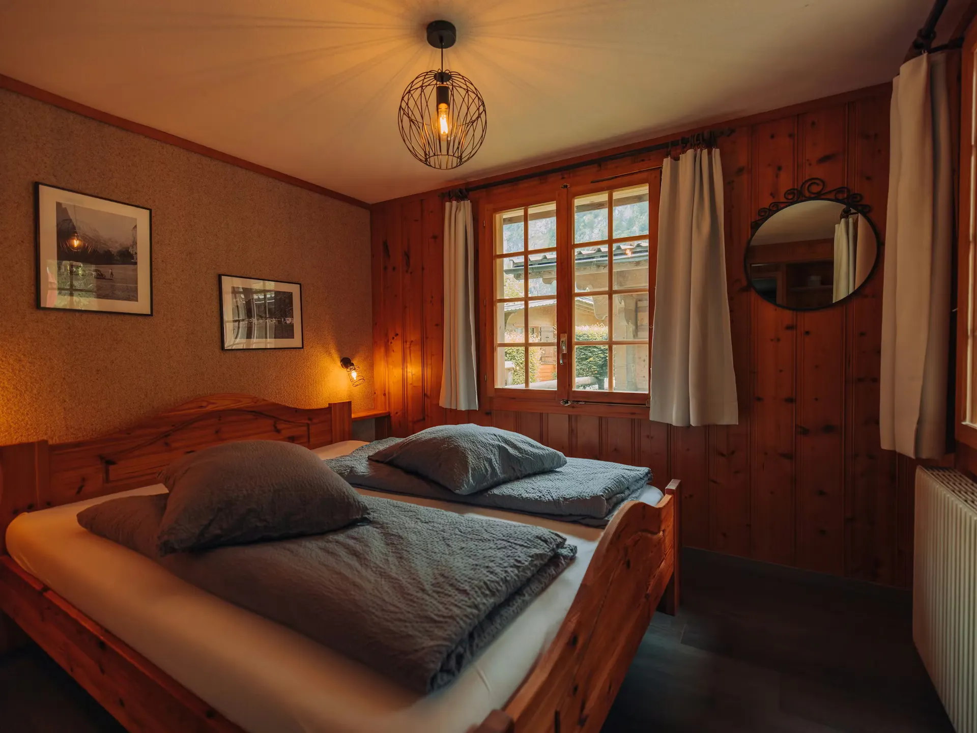 Schlafzimmer im Bungalow mit Doppelbett, grauen Laken und zwei alten gerahmten Fotos an der Wand