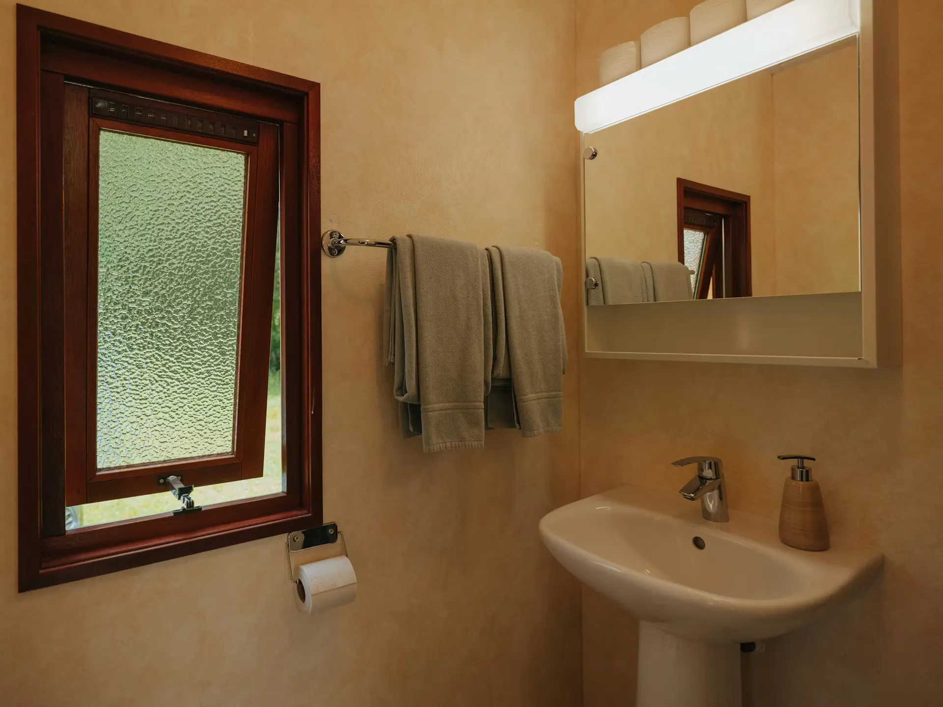 Badezimmer des Mobilheims Jungfrau mit einem Waschbecken und einem kleinen Fenster an der Seite, zwei Handtücher hängen an der Wand