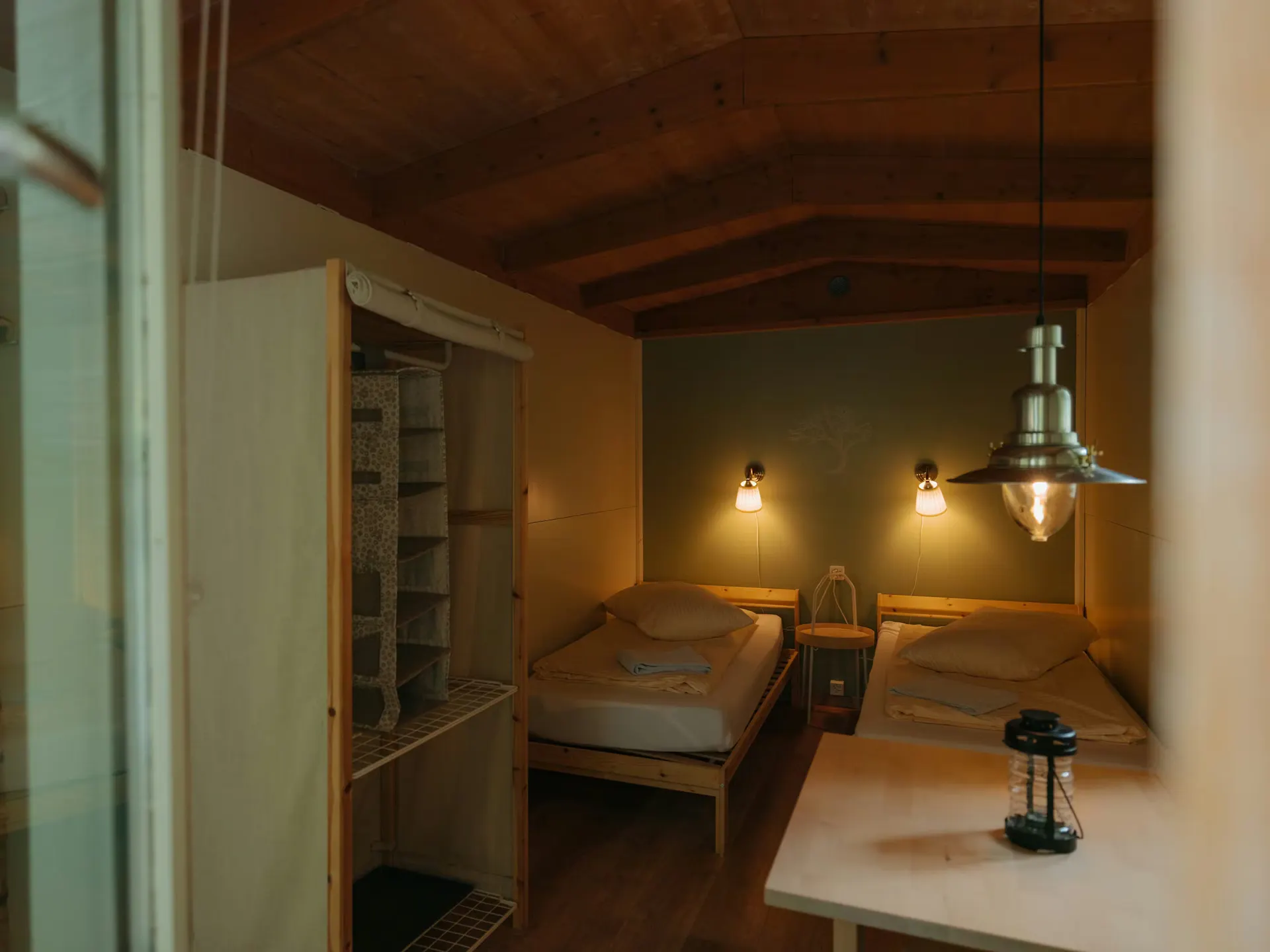Im Inneren der Fuchsbau Mietunterkunft mit zwei Betten, einem Tisch und einer kleinen Garderobe, zwei Lichter an der Wand oberhalb der Betten sind eingeschaltet