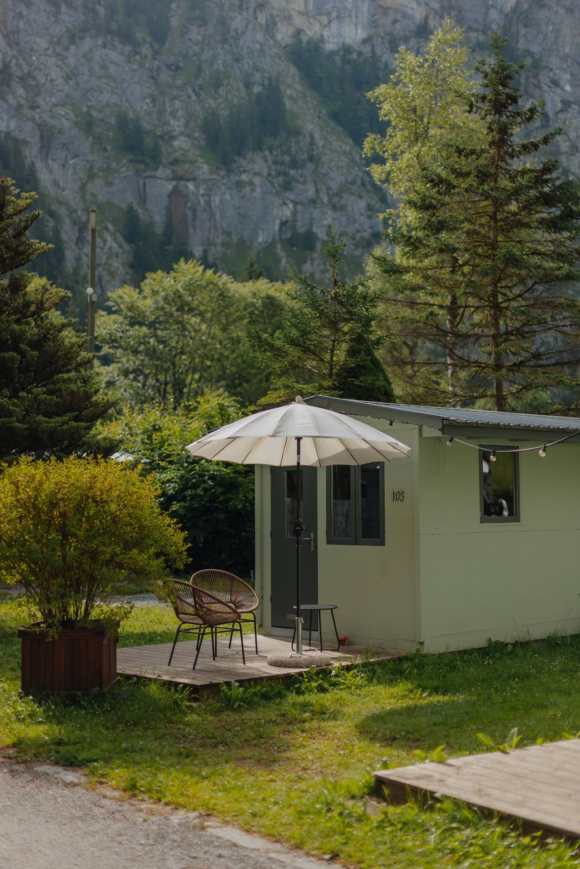 Fuchsbau Unterkunft mit Terrasse, Stühlen, einem Tisch und einem Sonnenschirm umgeben von grünem Gras und Bäumen