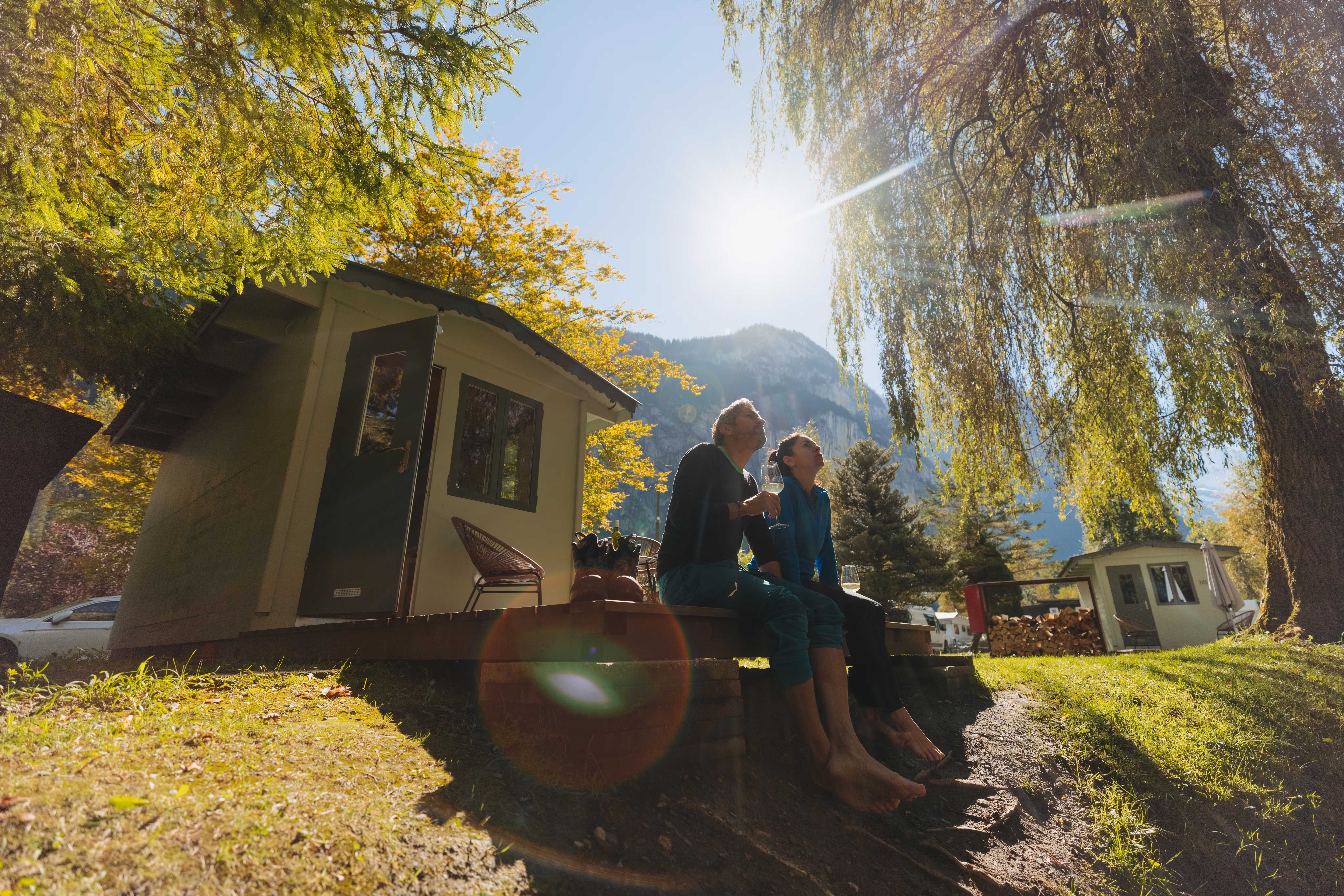 Paar sitzend auf der Terrasse vor der Fuchsbau Unterkunft auf dem Camping Jungfrau mit der scheinenden Sonne im Hintergrund