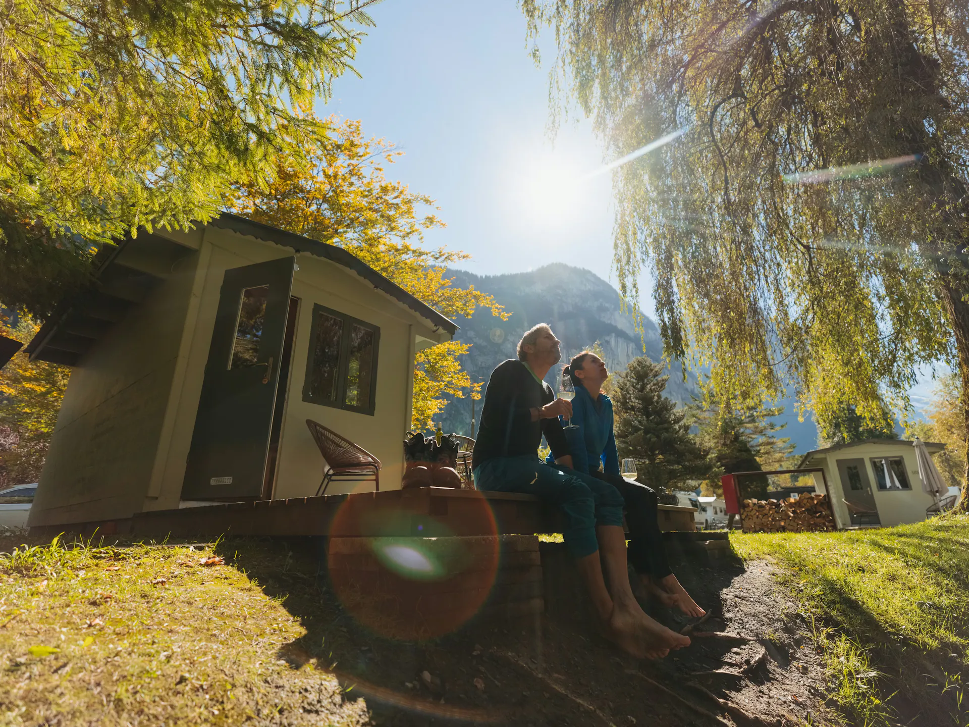 Paar sitzend auf der Terrasse vor der Fuchsbau Unterkunft auf dem Camping Jungfrau mit der scheinenden Sonne im Hintergrund