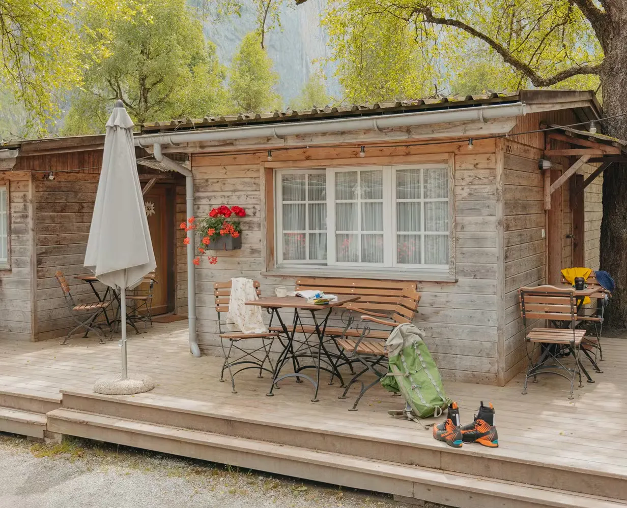 Mietunterkunft Familienhütte mit Stühlen und Tischen auf der Terrasse, mit Wanderausrüstung einschliesslich eines Rucksacks und Stiefeln