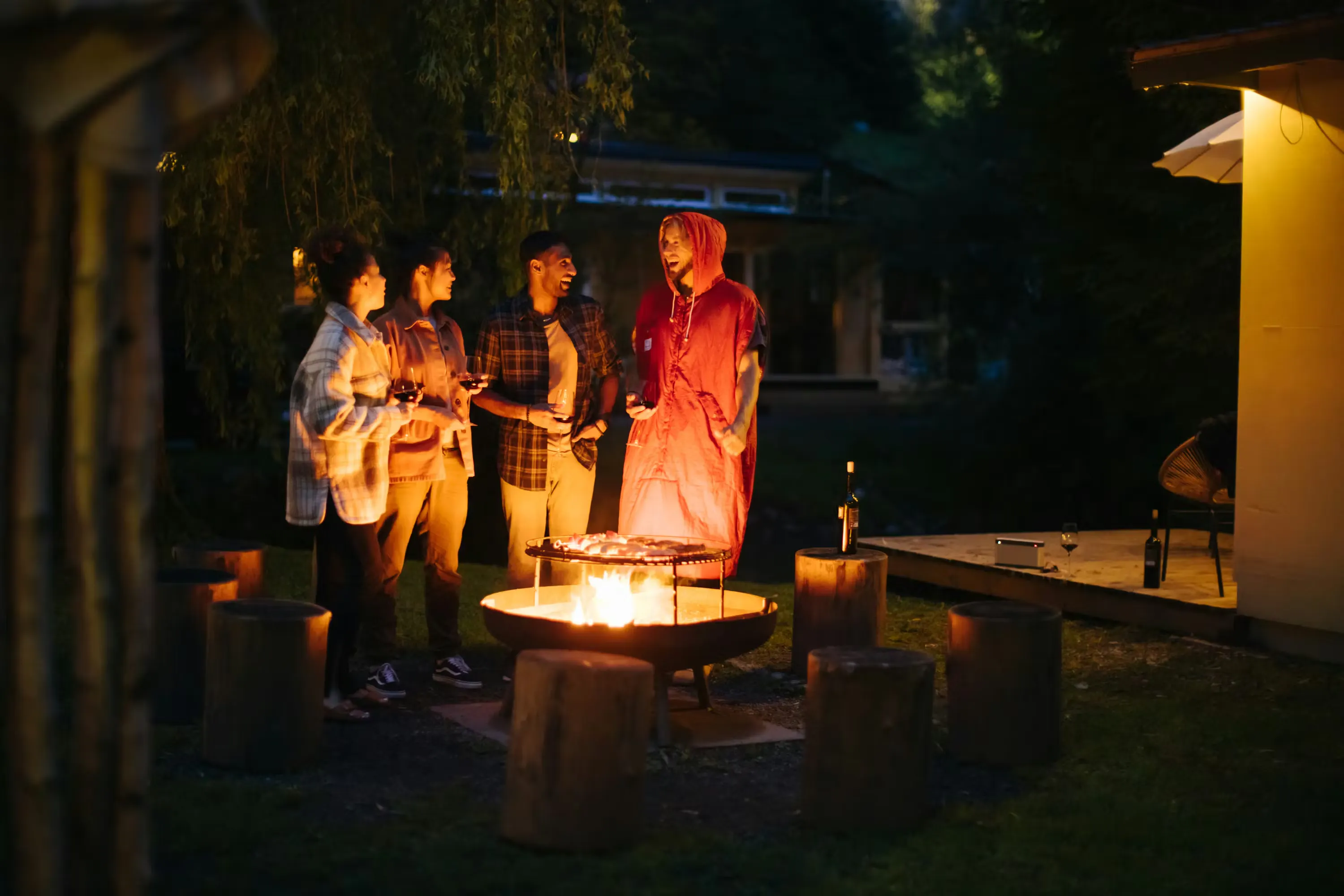 vier Freunde stehen um ein Feuer und grillen bei Dunkelheit