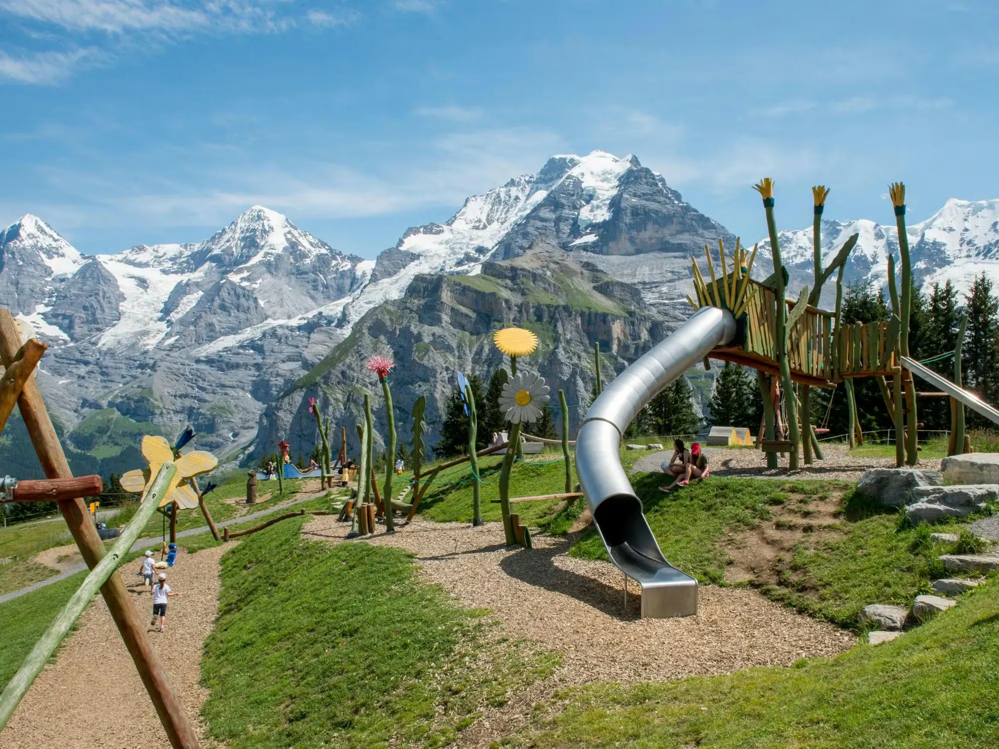 Bergspielplatz Flowerpark mit grossen Holzblumen und Bergen im Hintergrund