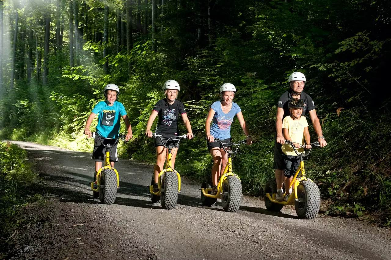 Familie fährt mit Monster-Trottis einen Waldweg hinunter