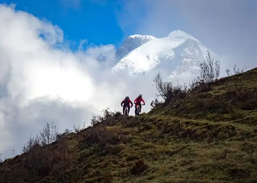 zwei Mountainbiker auf einem Bergpfad mit grossen schneebedeckten Bergen im Hintergrund