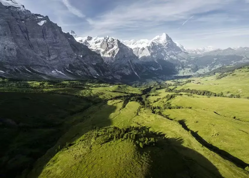 Drohnenansicht des Grindelwaldtals mit steilen Bergen auf der linken Seite und grünen Wiesen