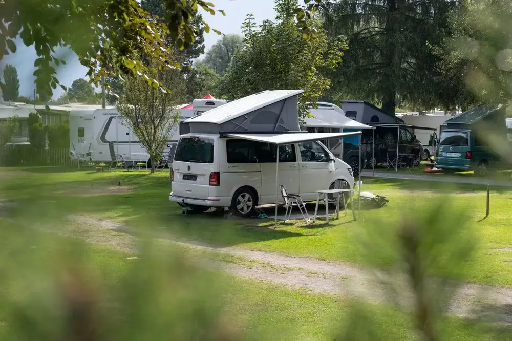 VW van auf dem Classic Stellplatz mit offenem Aufstelldach und Sonnensegel auf grünem Gras auf dem Camping Alpenblick