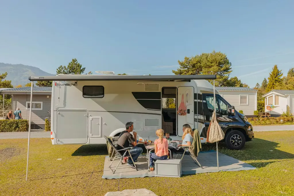 Wohnmobil mit Familie unter dem Vordach mit blauem Himmel dahinter