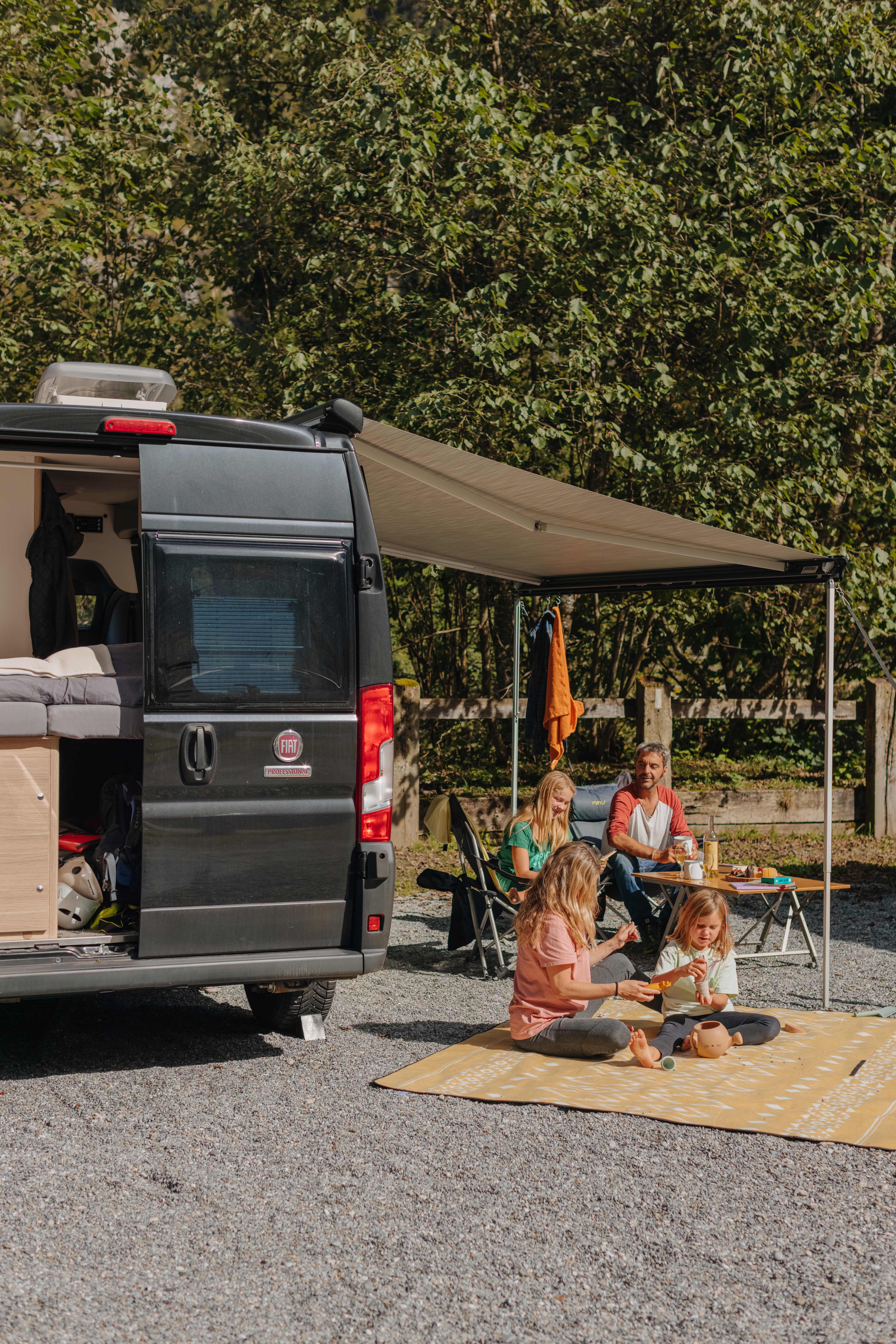 Sprinter auf einem Stellplatz auf dem Camping Jungfrau mit einer Familie auf einer Decke und Campingstühlen