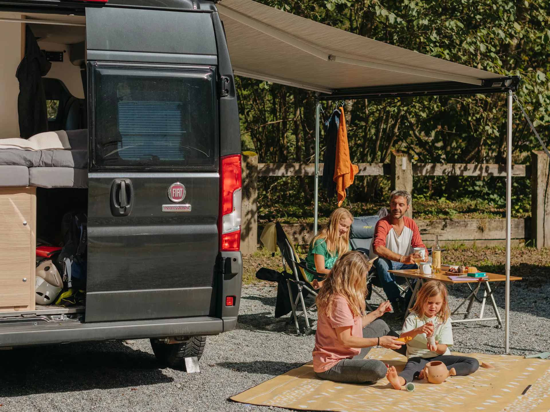 Sprinter auf einem Stellplatz auf dem Camping Jungfrau mit einer Familie auf einer Decke und Campingstühlen