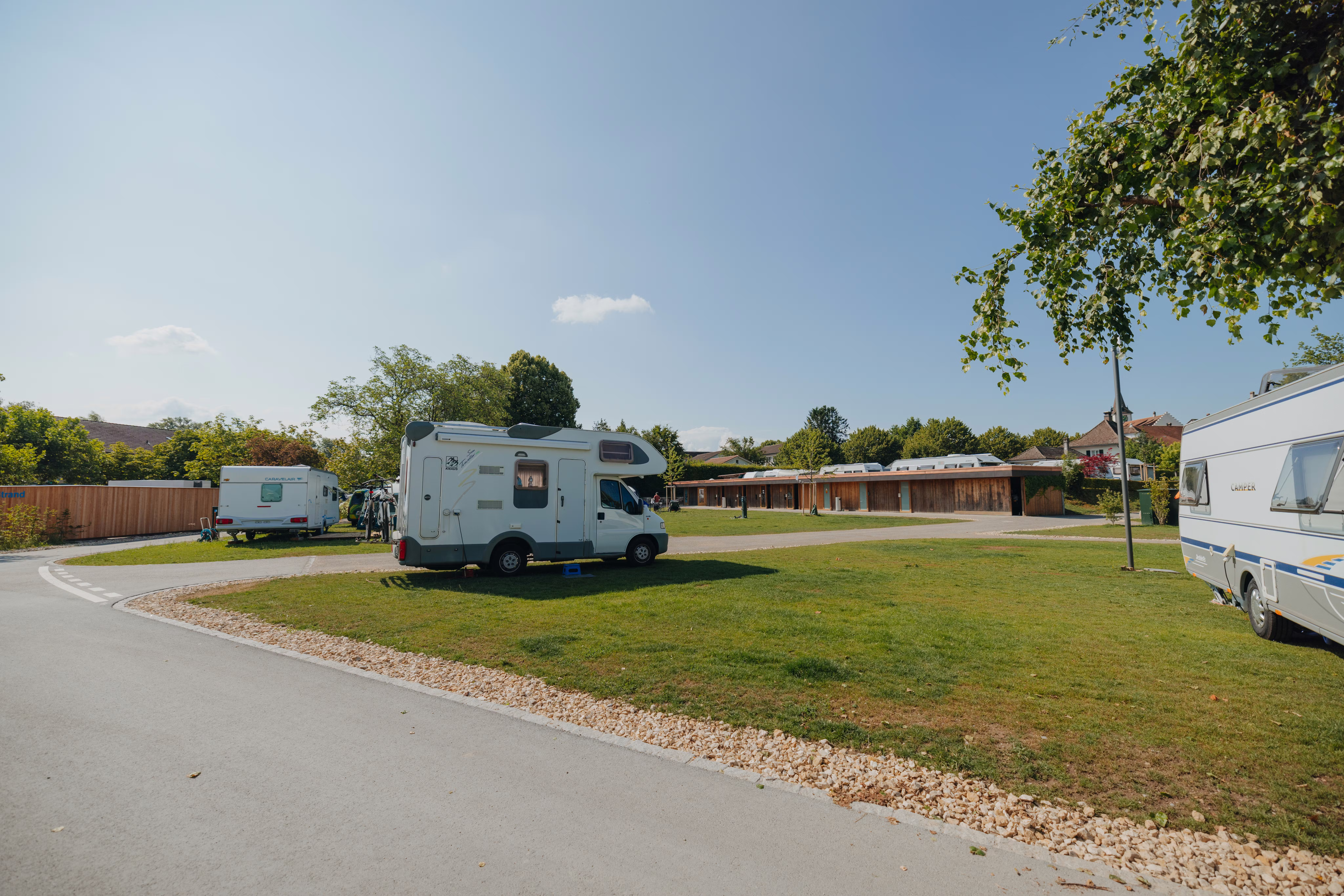 Wohnmobil auf einem Stellplatz Classic am See mit grünem Gras darunter und sanitären Anlagen im Hintergrund
