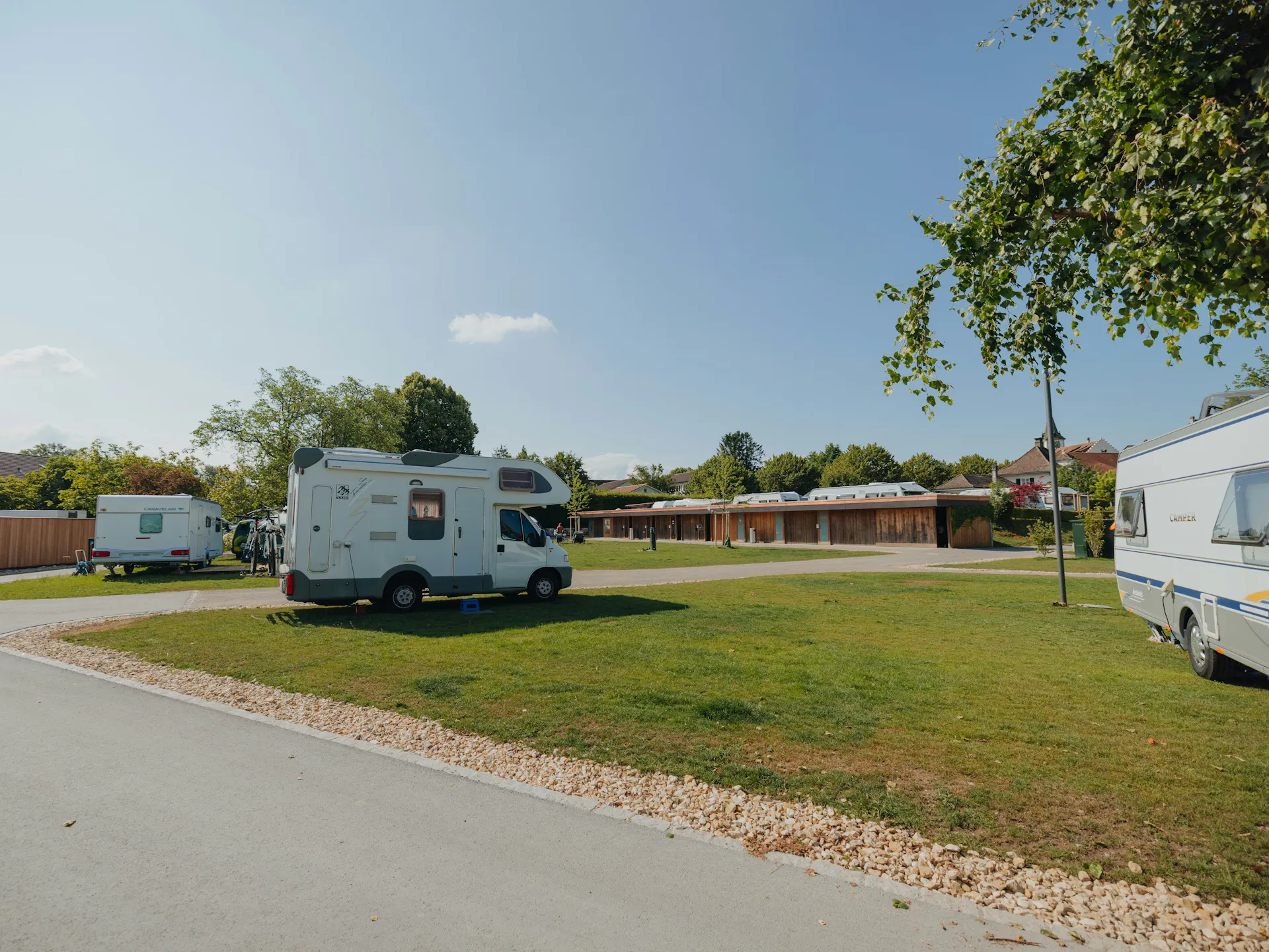 Wohnmobil auf einem Stellplatz Classic am See mit grünem Gras darunter und sanitären Anlagen im Hintergrund