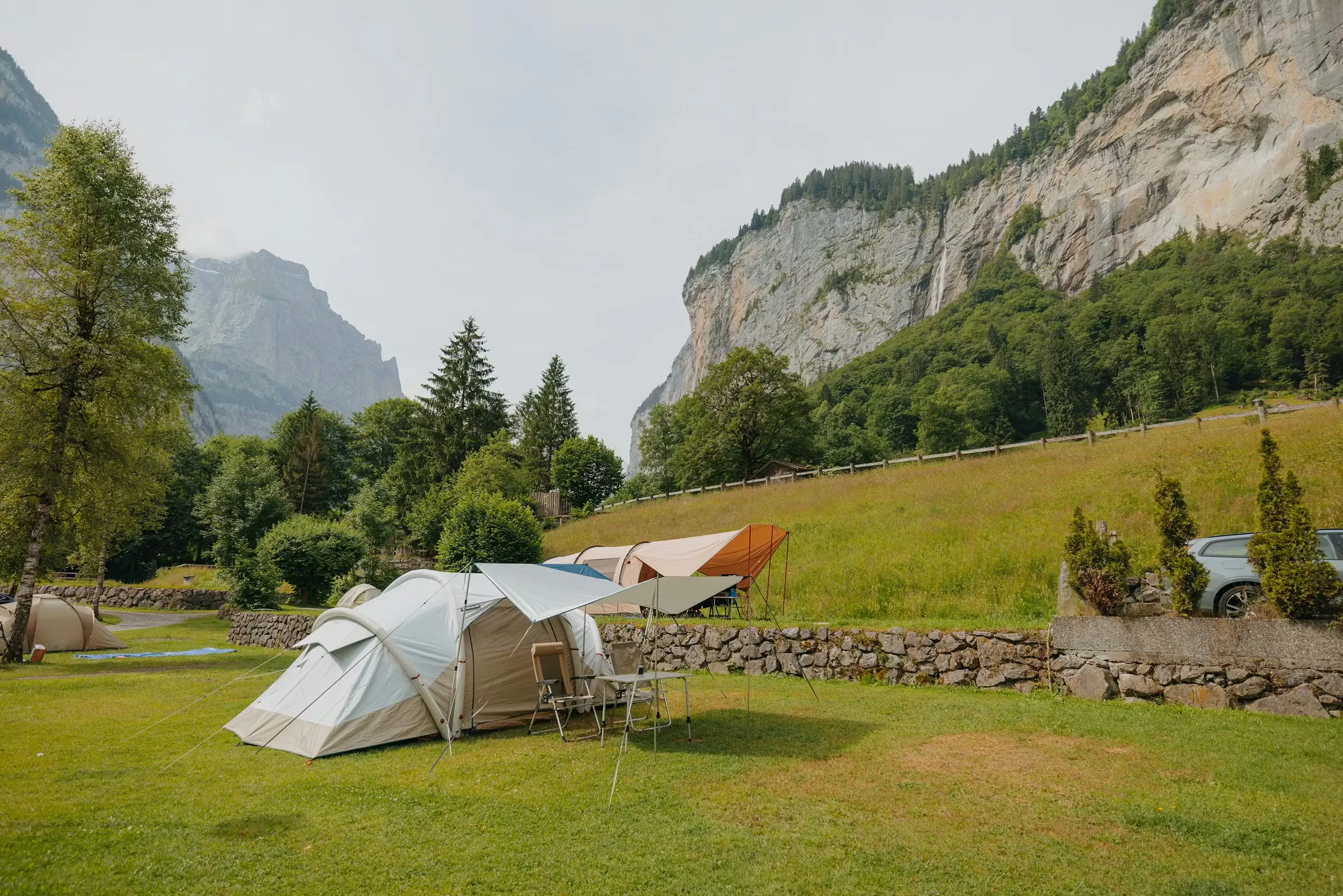 Zelte auf Zeltplätzen auf dem Camping Jungfrau mit Bergen und steilen Felswänden im Hintergrund sowie Wasserfällen