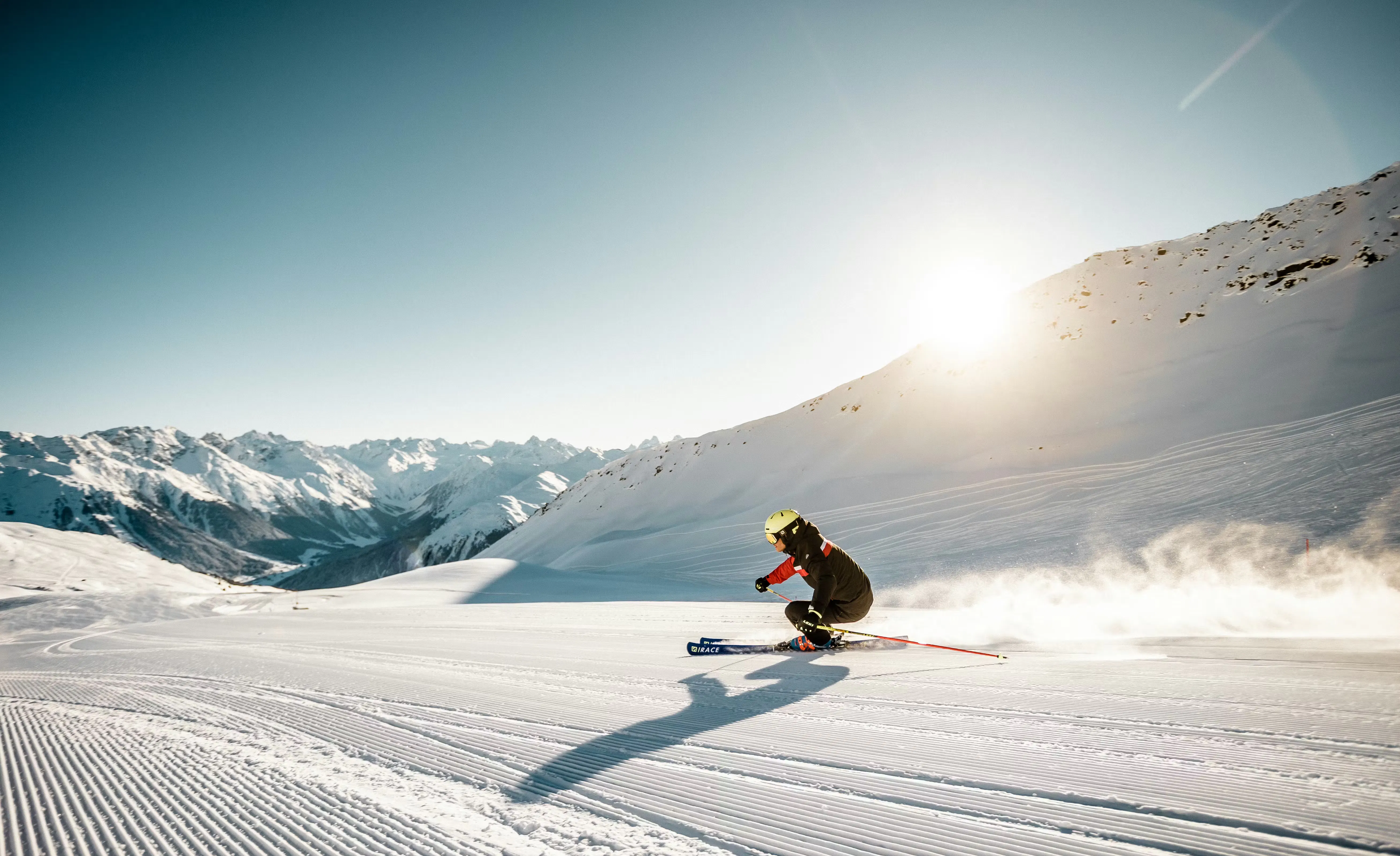 Skifahrer fährt im Skigebiet Parsenn Davos Klosters eine frische Piste runter mit Sonne im Hintergrund