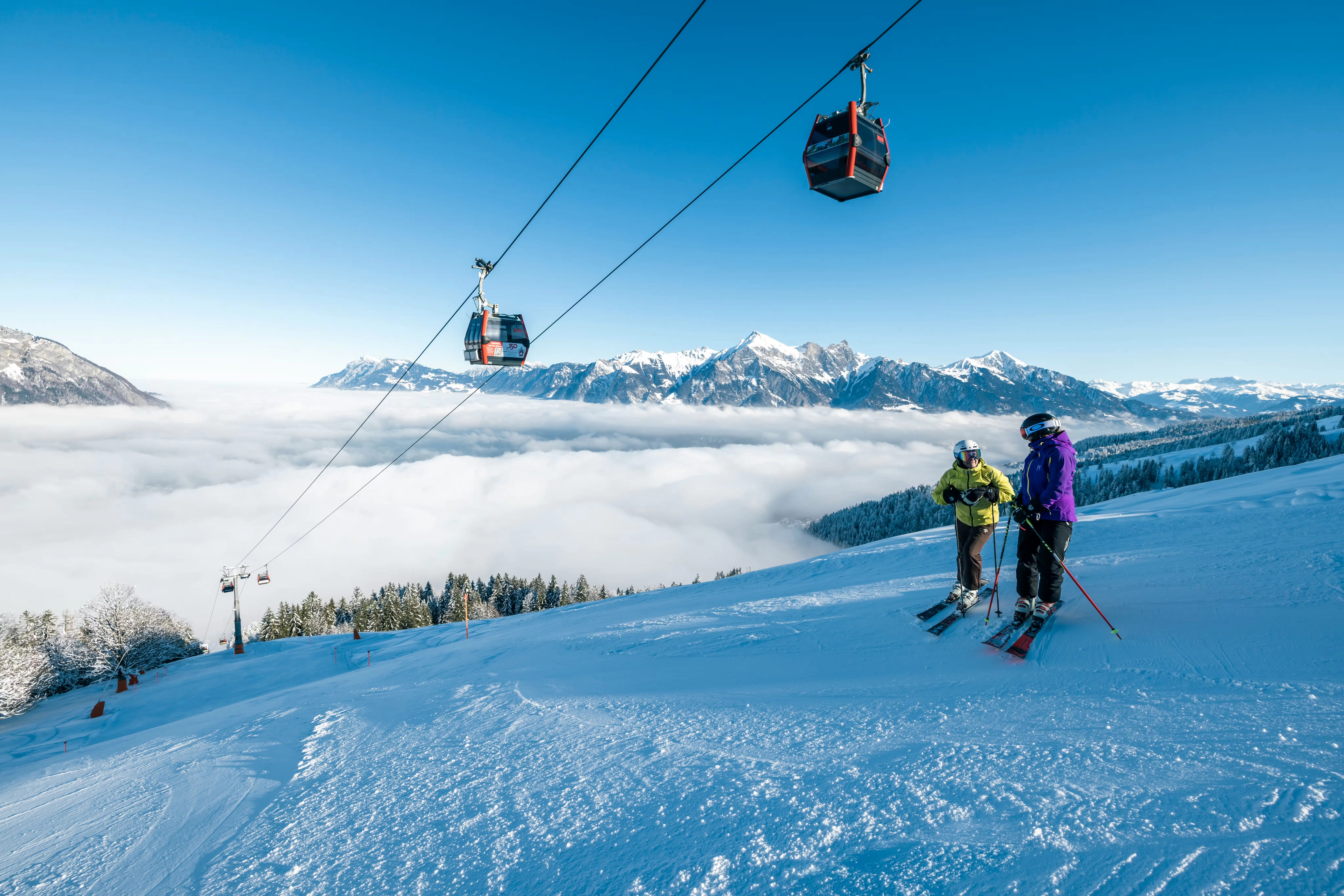 Zwei Skifahrer auf der Piste im Pizol Skigebiet mit Gondelbahn über ihnen und schönem Wetter
