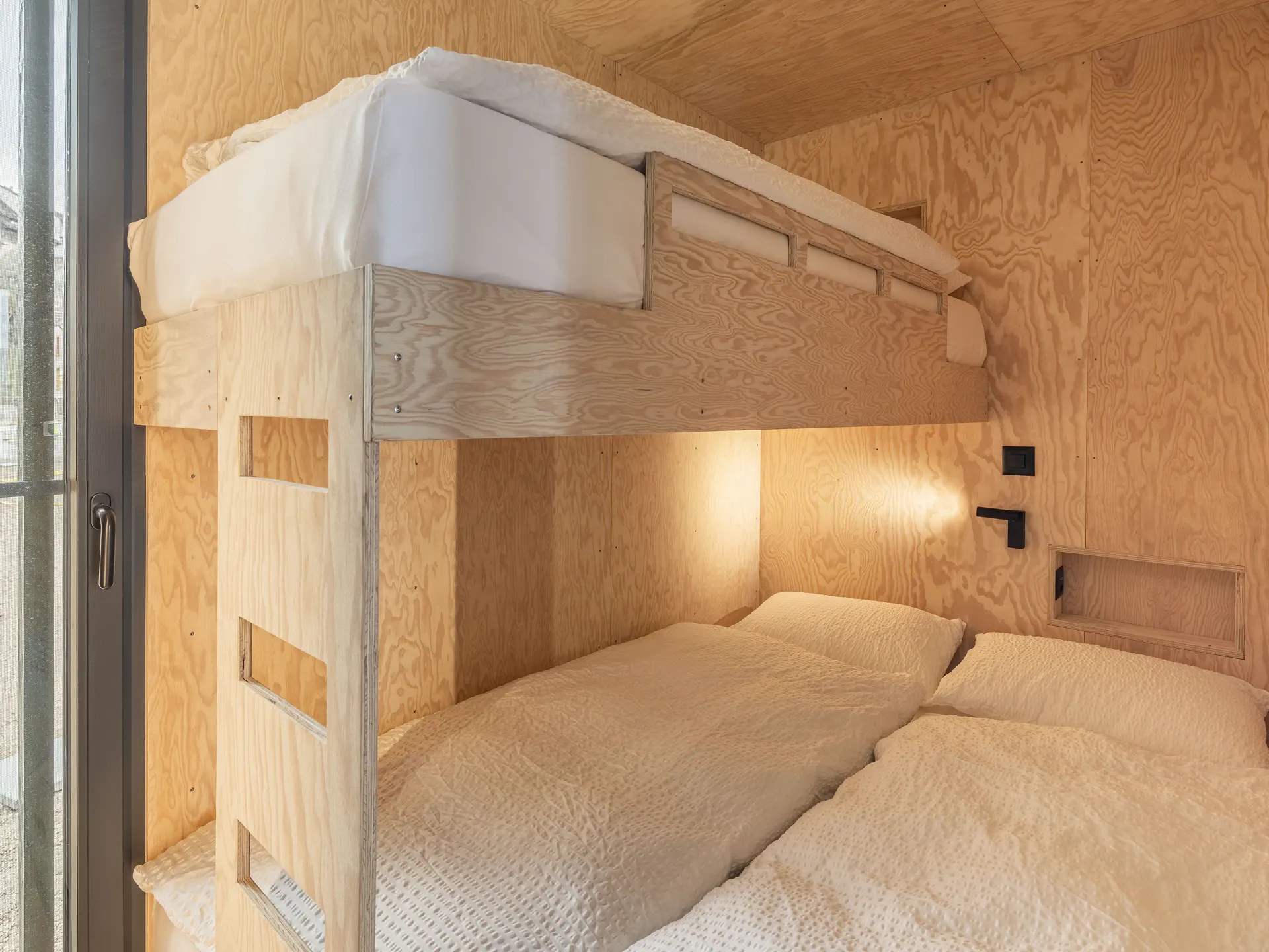 Doppelbett mit Einzelbett obenauf aus Holz in der Beach Cottage Mietunterkunft auf dem Camping Erlach mit weisser Bettwäsche