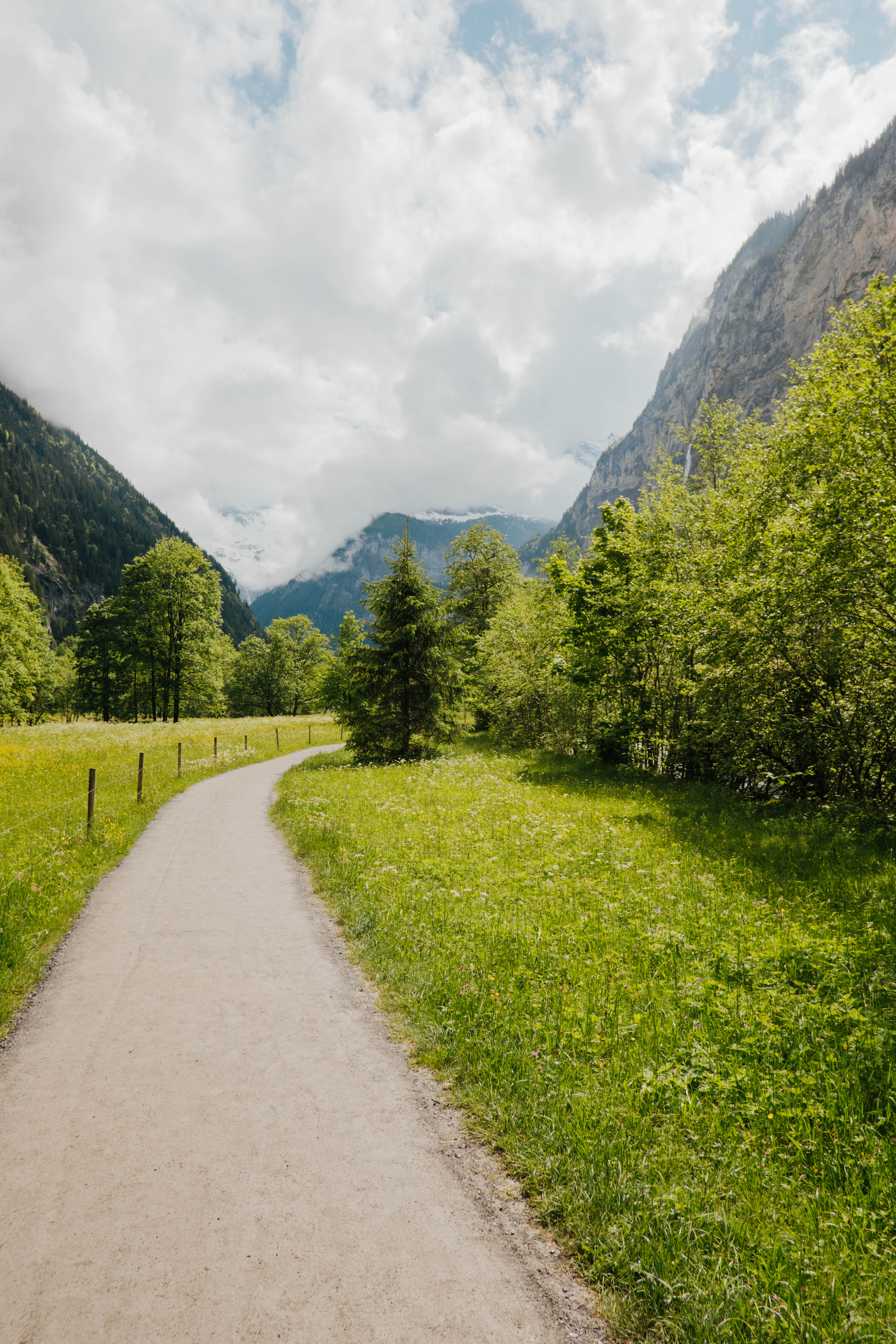Spazierweg im Lauterbrunnental zwischen Felswänden umgeben von grünen Büschen, Bäumen und Wiesen
