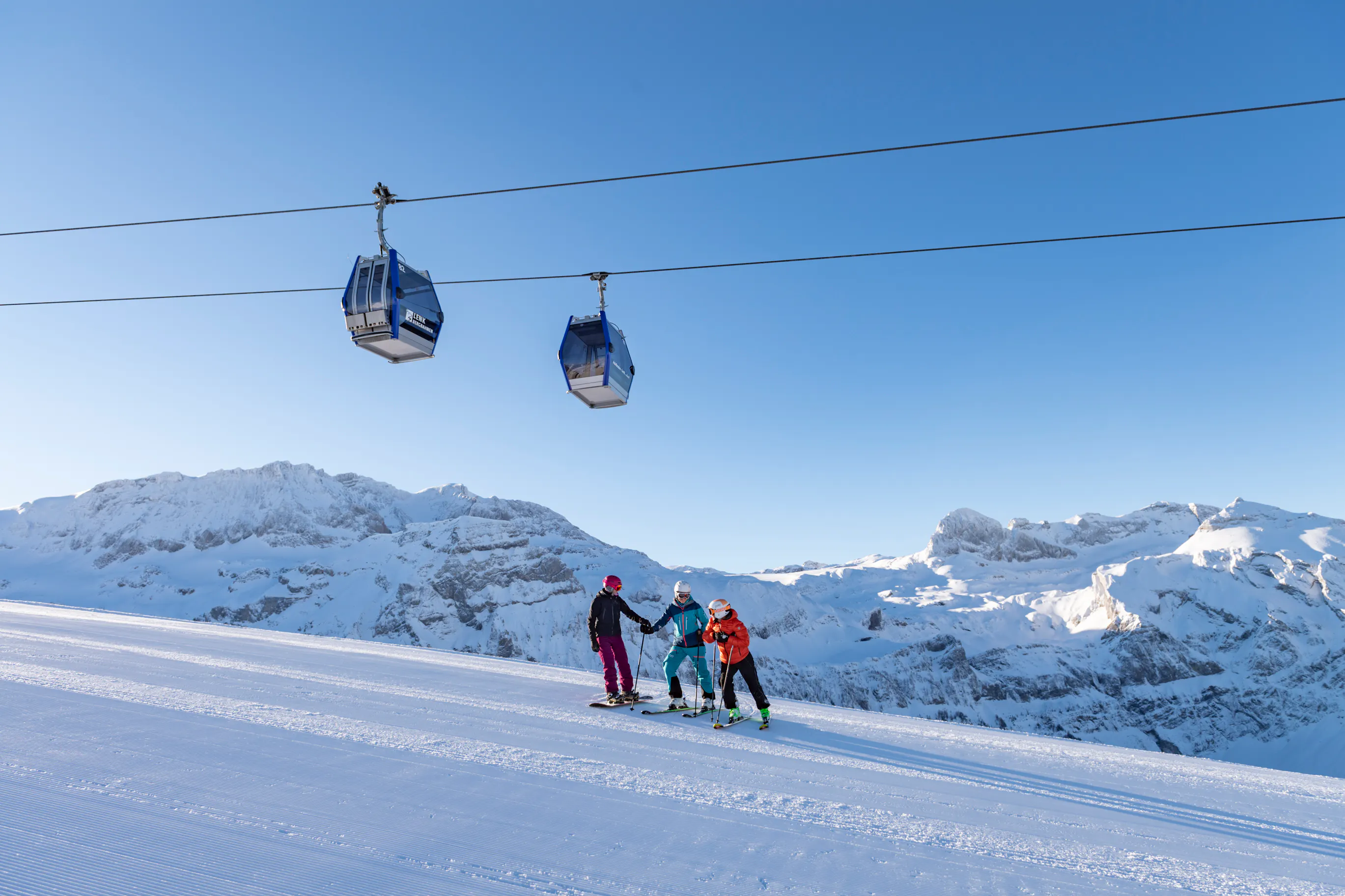Drei Skifahrer auf einer Skipiste in Adelboden-Link mit Gondeln über der Piste