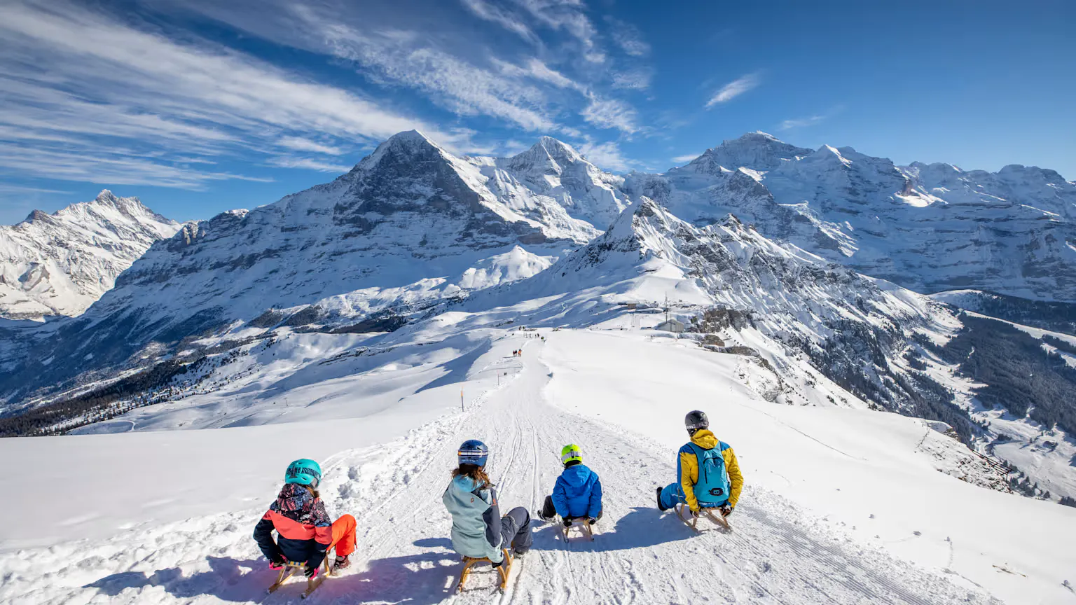 Vier Personen am Schlitteln mit Bergpanorama