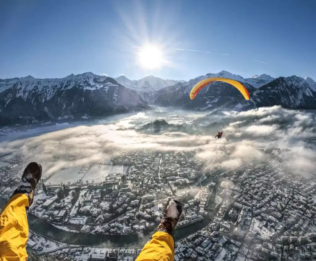 Gleitschirmflieger in der Luft über dem winterlichen Interlaken mit ein paar Wolken über der Stadt und den Berner Alpen im Hintergrund