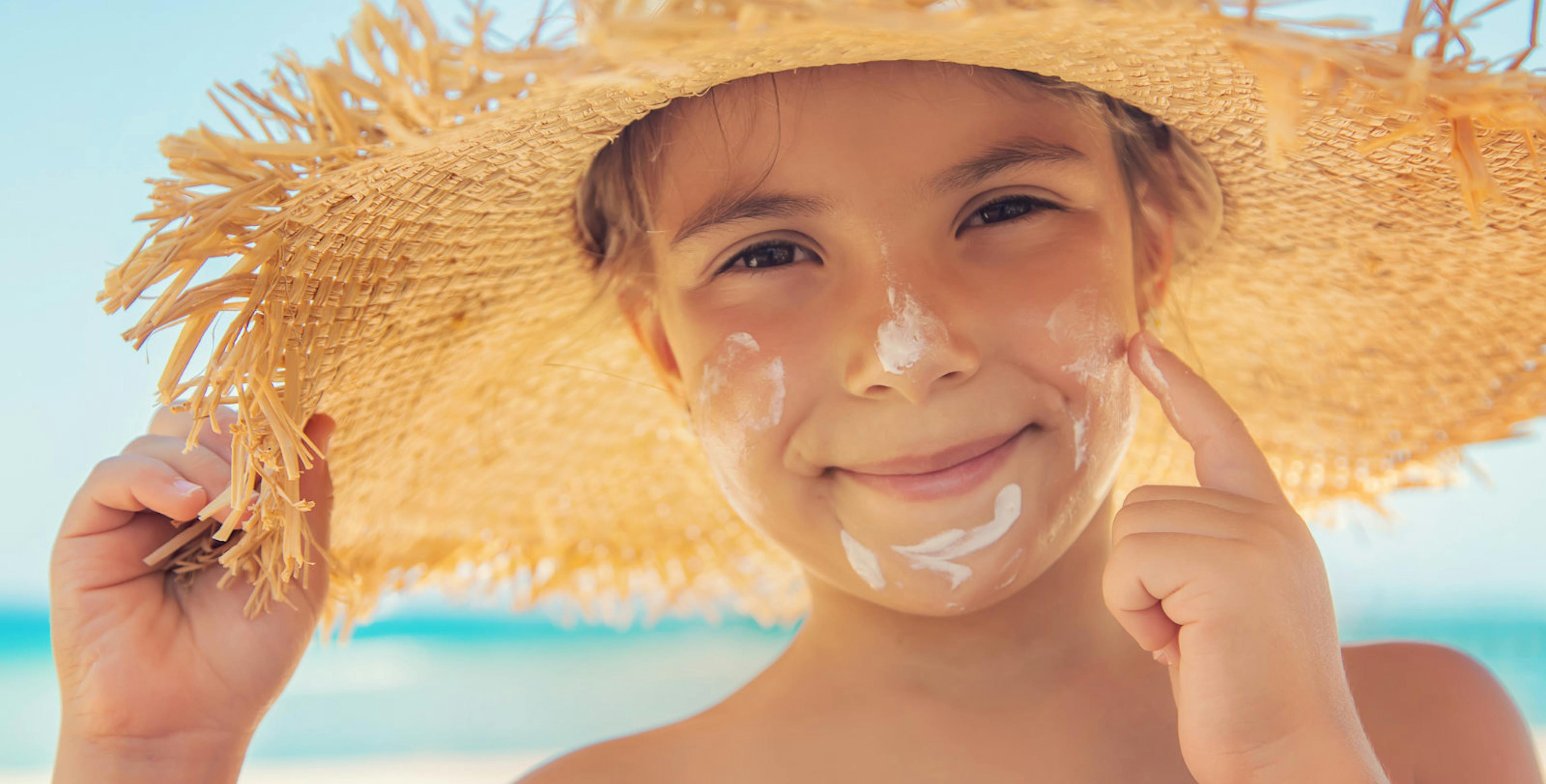 Boy in straw sun hat wearing sunscreen