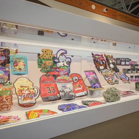 Colorful, branded cannabis product packaging displayed inside a well-lit counter case at Cannavine Ukiah. Includes edibles, flower pouches, concentrates, and jars, with a staff member visible in the background.